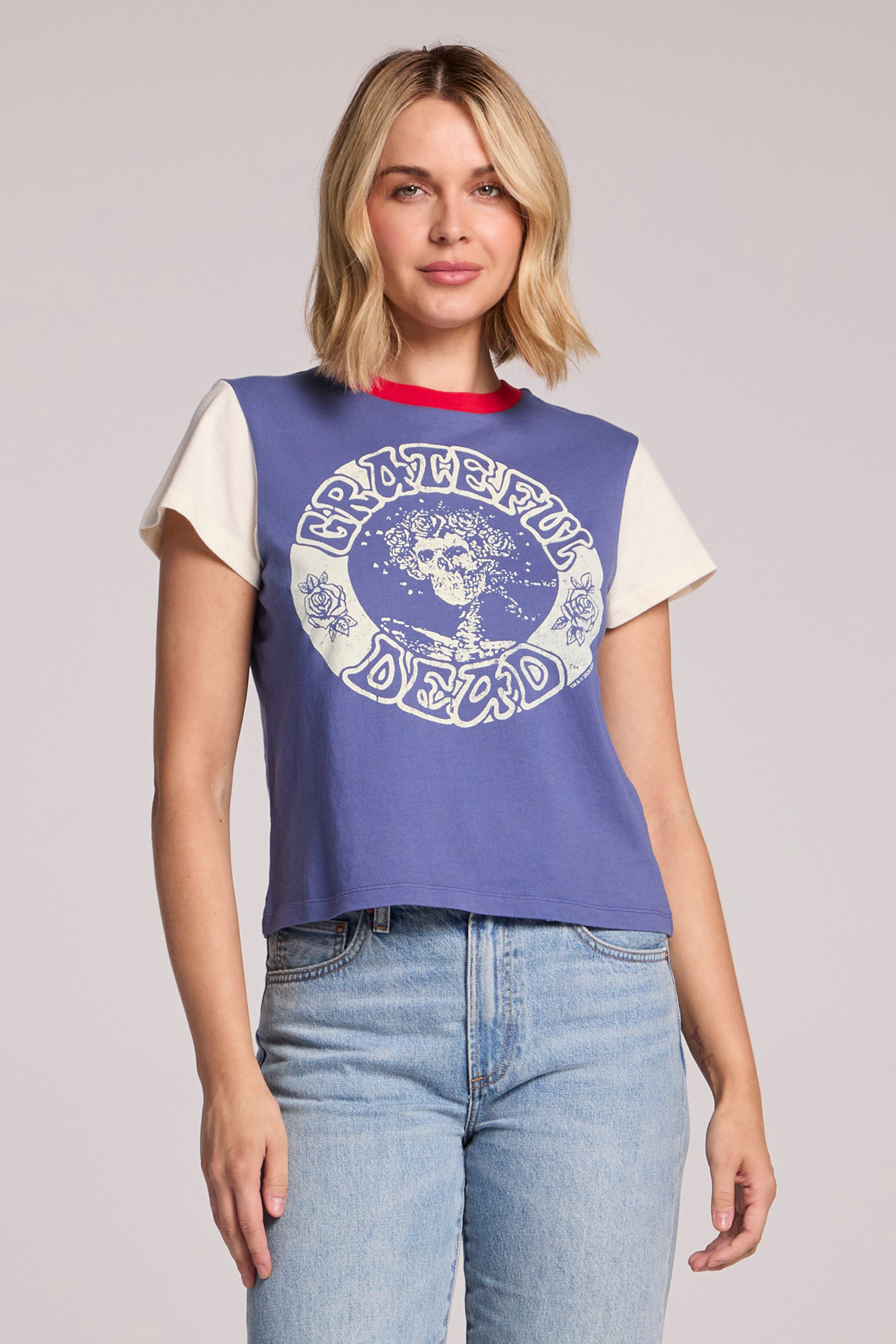 A woman with blonde hair wears the Chaser Grateful Dead - Classic Bertha tee in Blue Multi, featuring a Bertha skull graphic, and light blue jeans, standing against a neutral background.