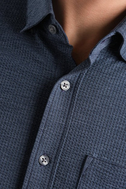 Close-up of a person wearing the South Moon Under Commuter Seersucker Short Sleeve Shirt in dark blue, featuring white buttons and a visible collar, upper chest, and partial chest pocket.