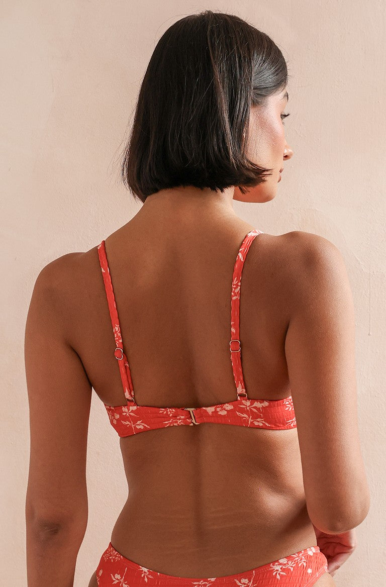 A woman with short dark hair is seen from behind wearing Dippin' Daisy's Zen Top in a red floral print with adjustable straps, standing against a light wall.