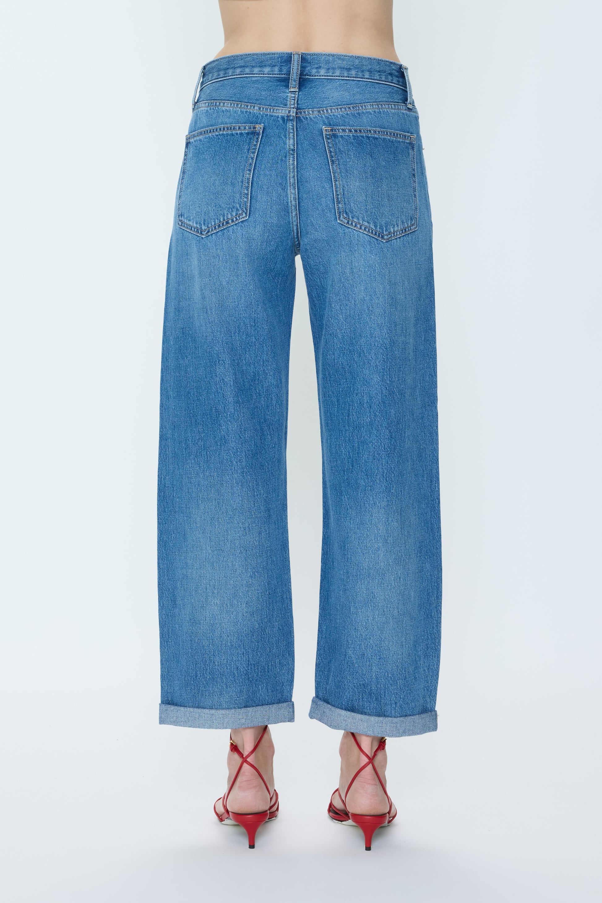 A person stands with their back to the camera, wearing Pistola Donny Rolled Hem Bf high-waisted wide-leg blue jeans with rolled cuffs and red strappy heels against a plain light background.