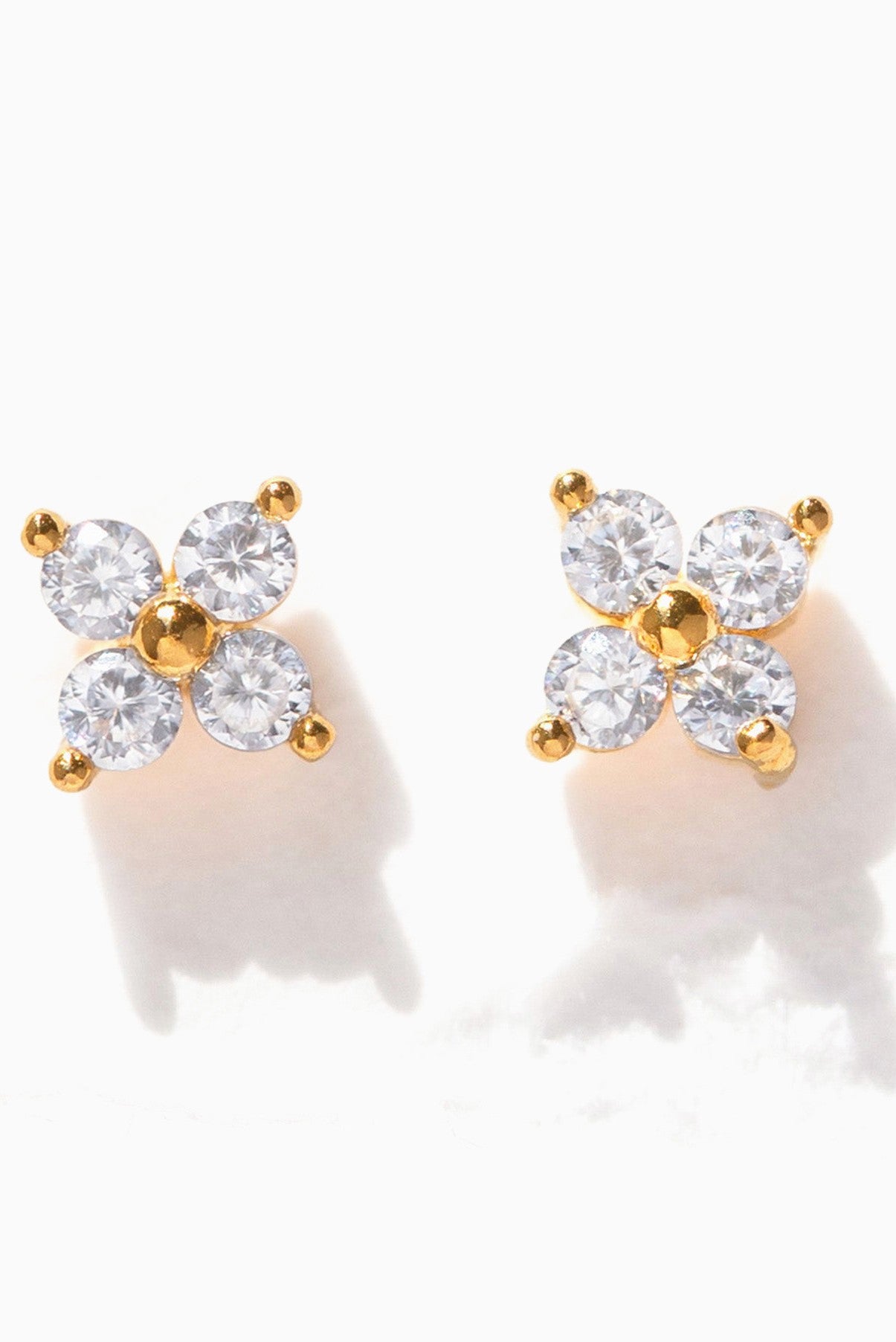 The Girls Crew Teeny Tiny Clear Cluster Studs feature four round cubic zirconia stones in a floral pattern with gold bead accents, all set on sterling silver posts.
