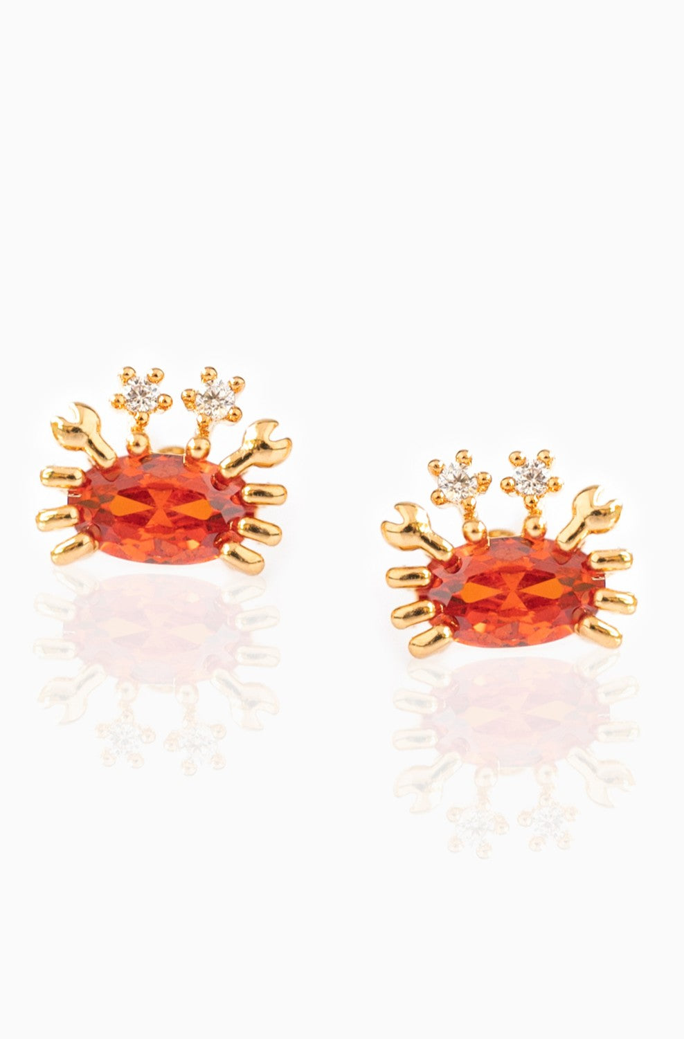Girls Crew’s Cutie Crab Stud Earrings feature 18k gold plating, sterling silver posts, an oval orange gemstone body, and sparkling cubic zirconia eyes. Shown against a white background.