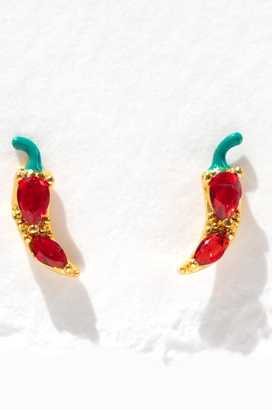 The Girls Crew Red Hot Chili Pepper Studs are 18k gold plated earrings with red cubic zirconia bodies and green tops, shown against a white textured background.