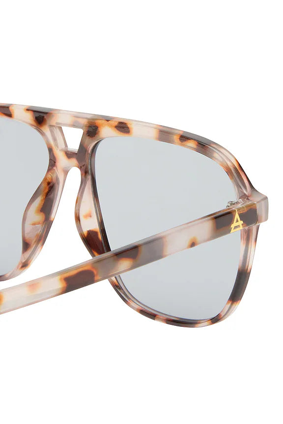 Close-up of Aire’s Aquarius Sunnies: cookie tort frame sunglasses with light lenses and a gold A logo on the temple.