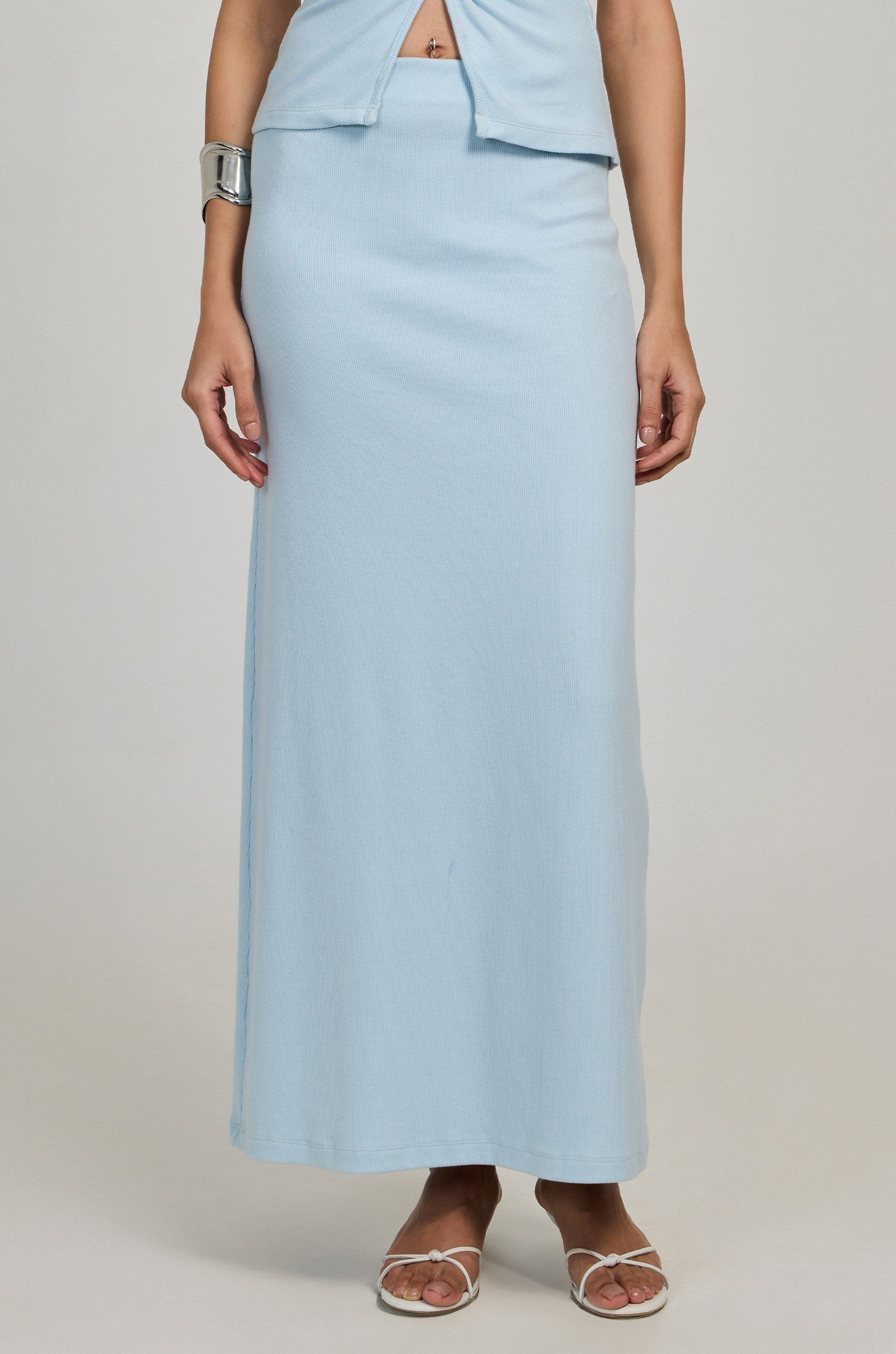 A person wearing the Summer Away Minato Skirt in blue with a matching sleeveless top, chunky silver bracelet, and white sandals stands against a neutral background.