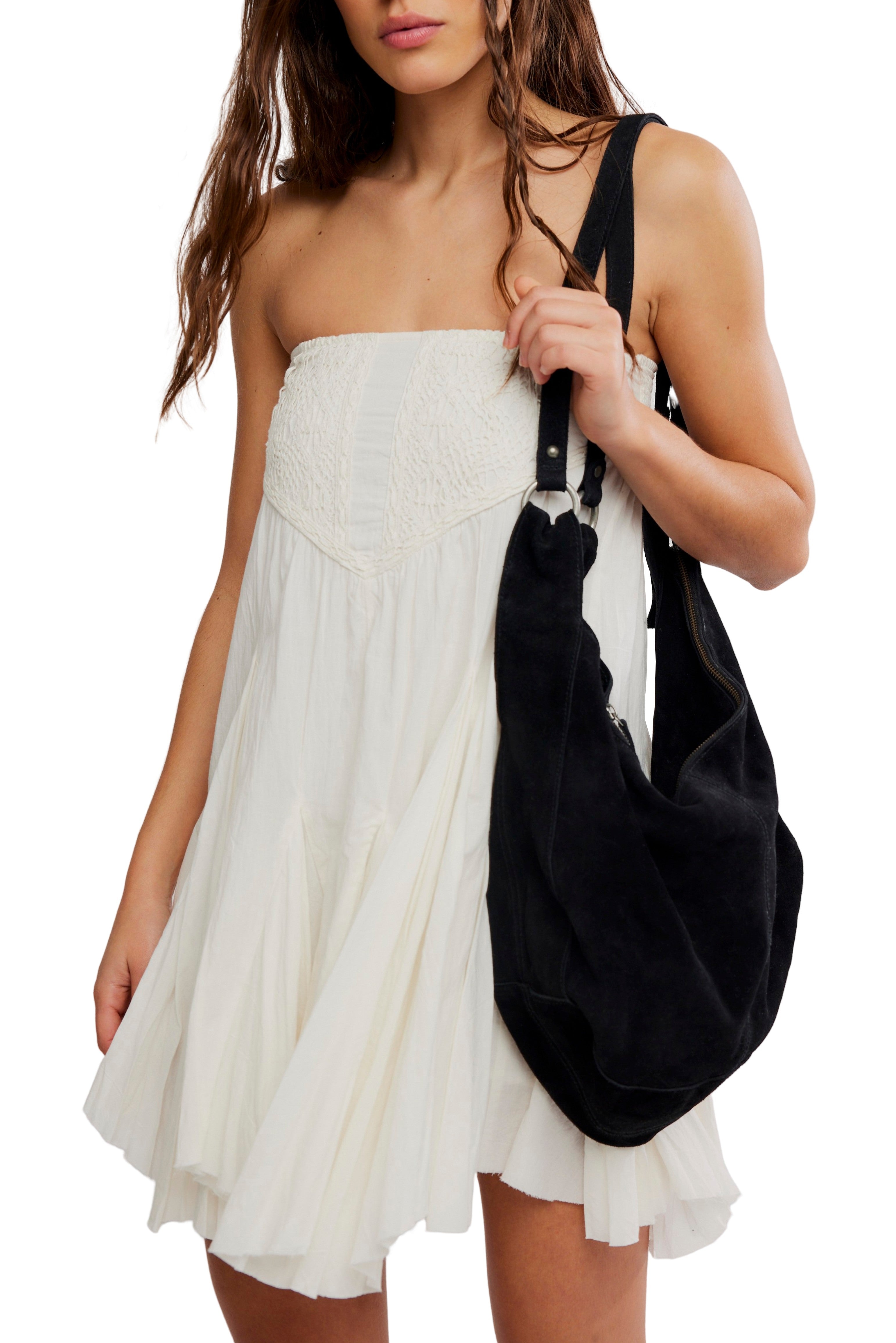 A woman in the Free People Fp 1 Frida Godet Midi Skirt, a strapless flowy white cotton style, holds a large black suede shoulder bag. Only her upper body appears against a white background.