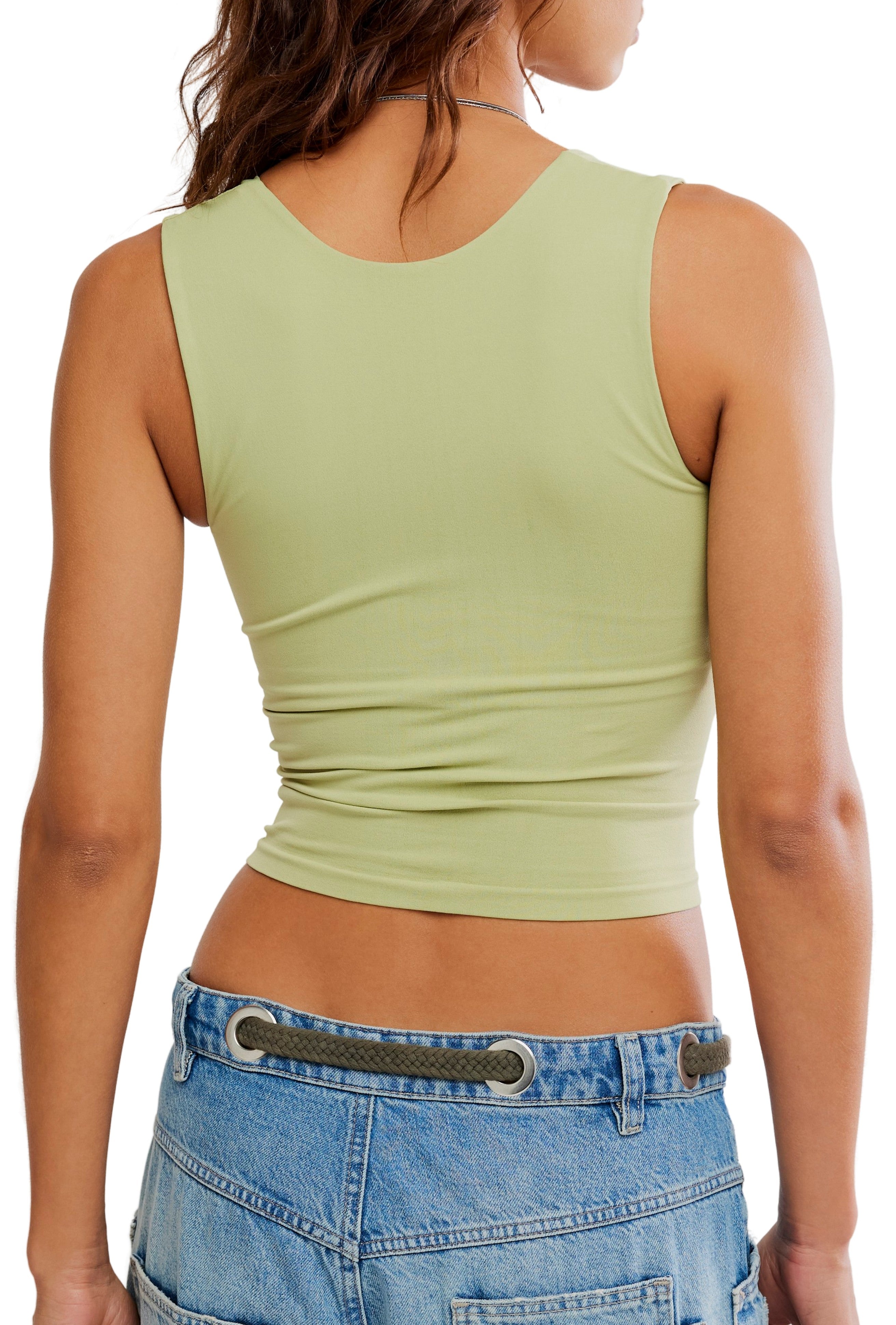 A person is shown from the back wearing the Free People Clean Lines Muscle Cami, a sleeveless light green crop top with an interior shelf bra, paired with light blue denim jeans and a belt featuring round metal grommets.