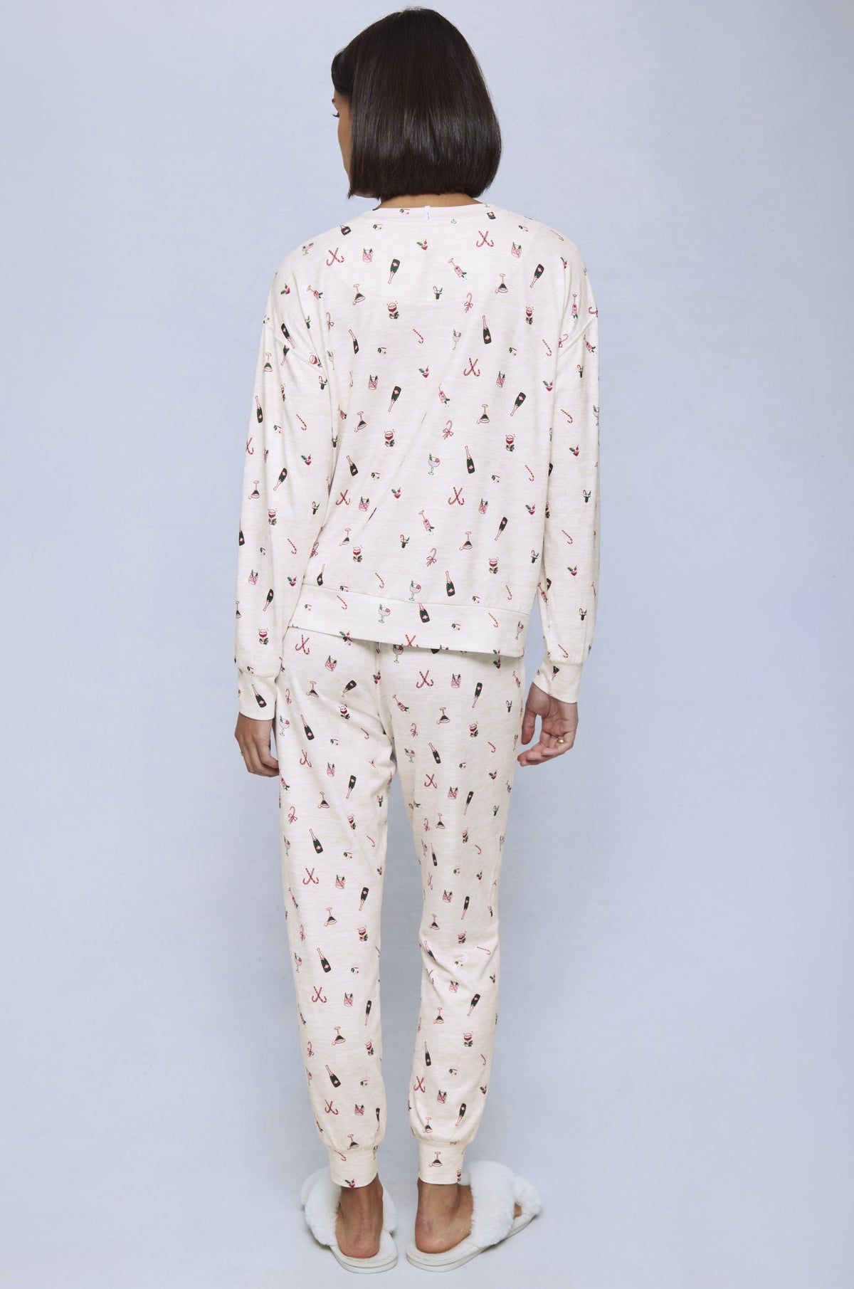Woman wearing cream jersey pajama set with red and black holiday cocktail print, shown from back.