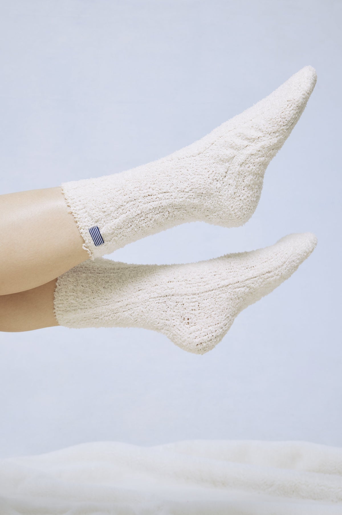 Pair of cream cable-knit socks with small striped detail at ankle, shown on feet against light background.