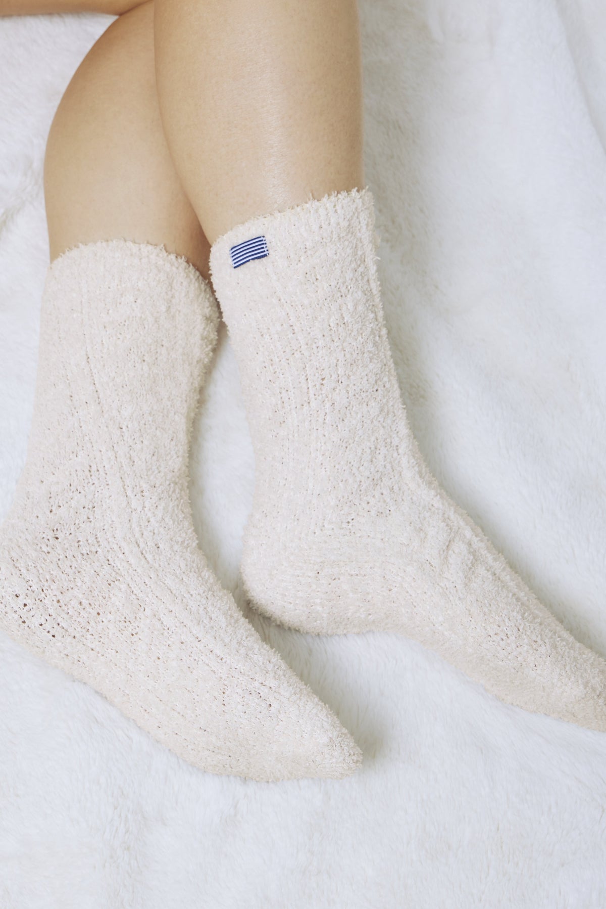 Cream cable-knit socks with blue stripe detail on cuff, worn on feet.
