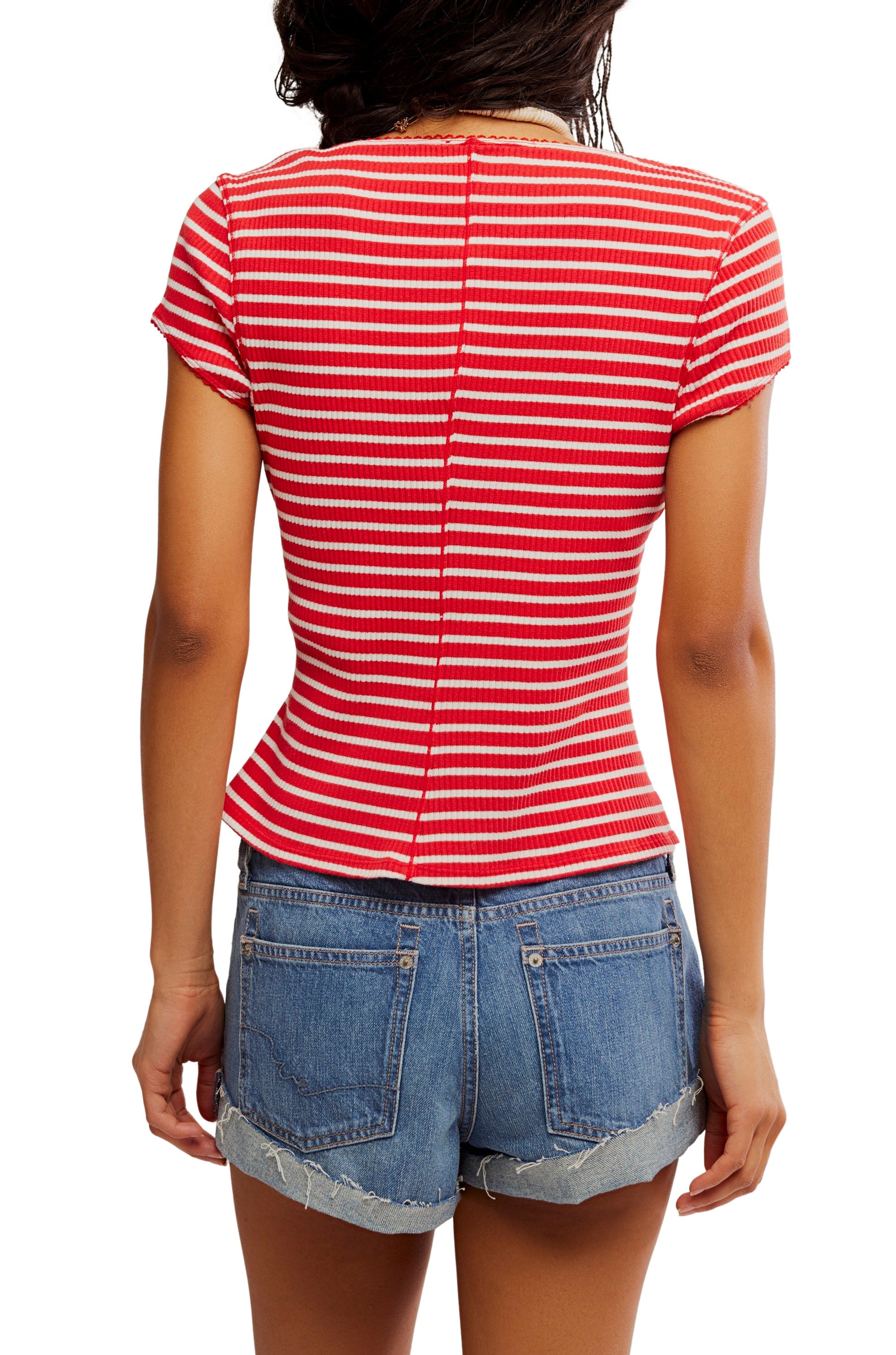 A person is seen from the back wearing Free People’s Most Wanted Striped Cardi in red and white, paired with blue denim shorts with frayed hems. The background is plain white.
