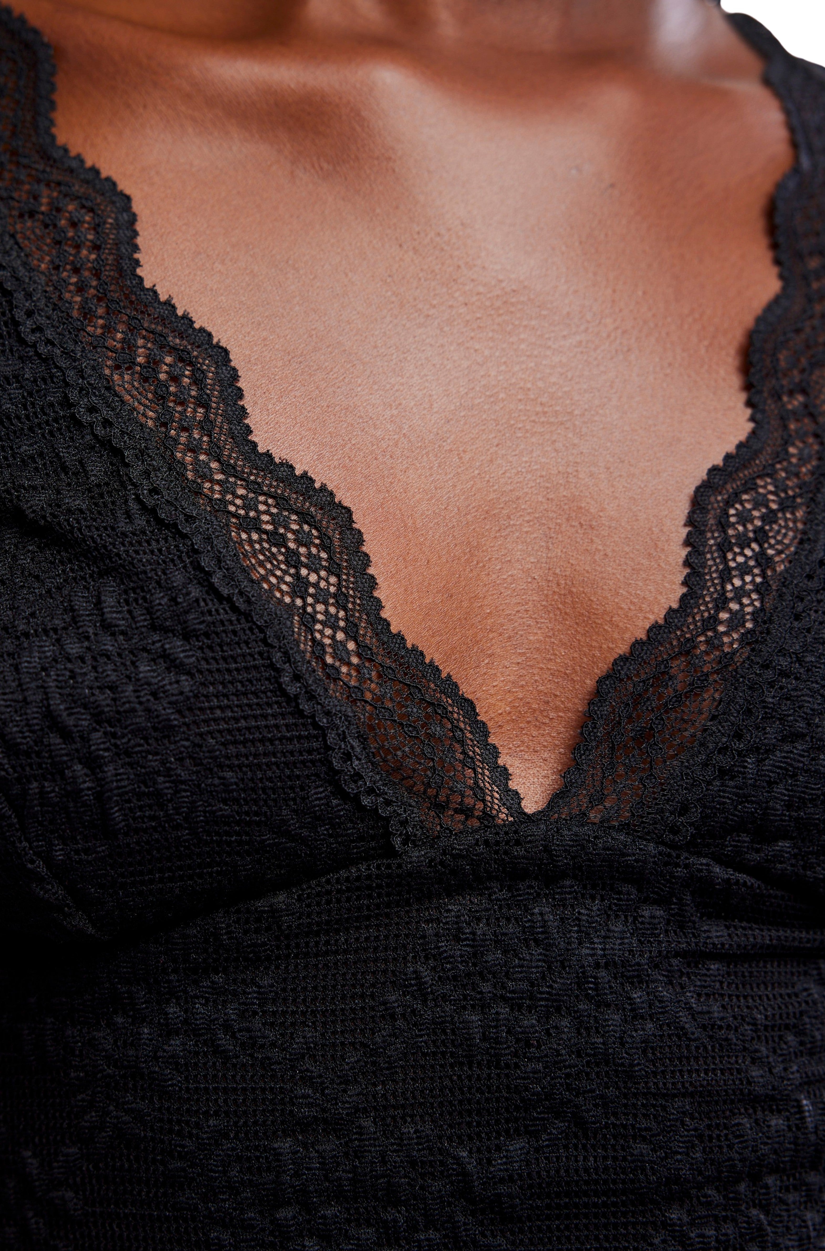 A close-up of a person wearing the Loved You First Lace by Free People, a black fitted garment featuring a deep V-neckline with scalloped lace trim, focusing on the chest and neckline.