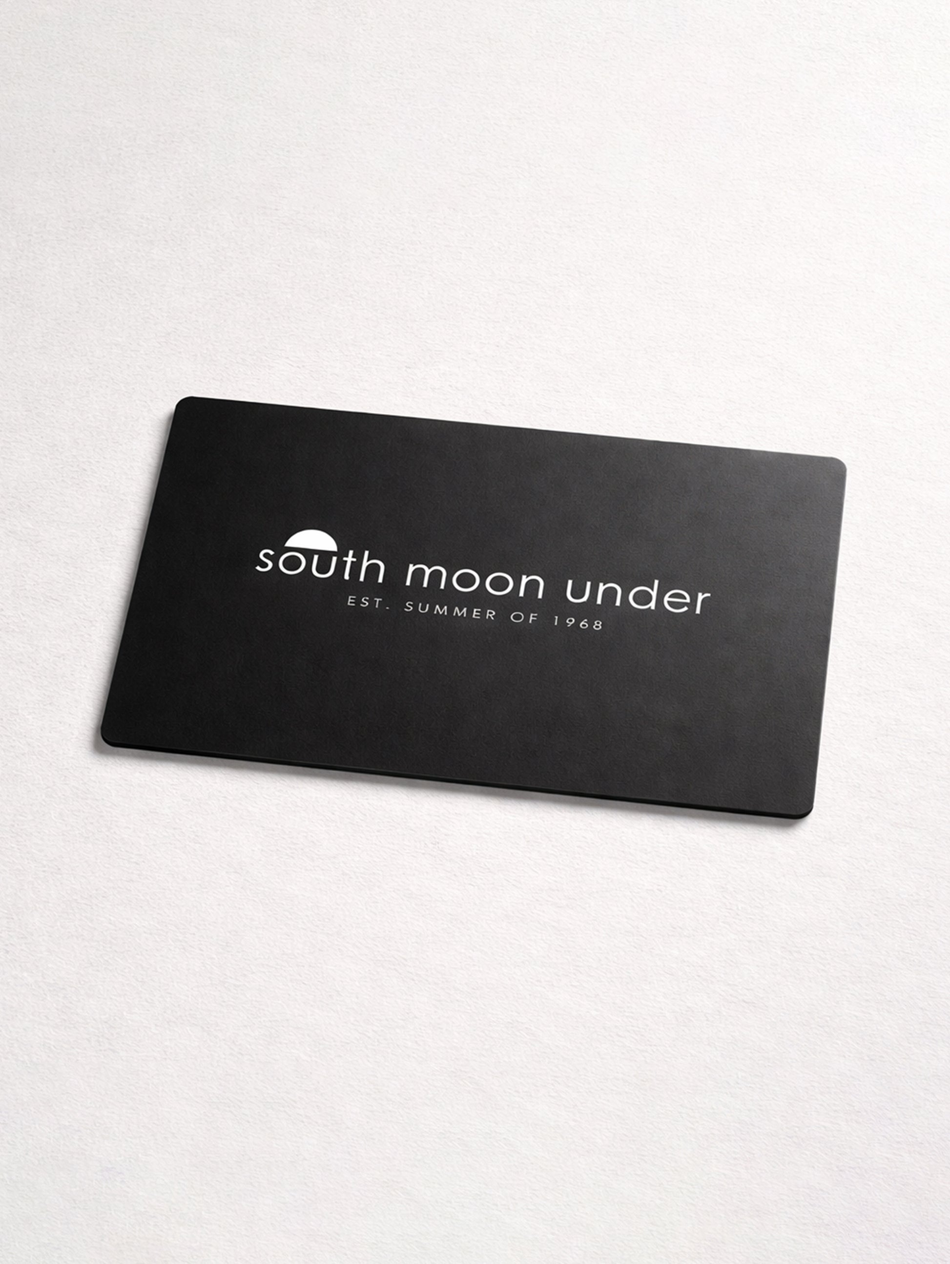 A black rectangular South Moon Under eGift Card with a white logo and "EST. SUMMER OF 1968" is centered on a light surface.