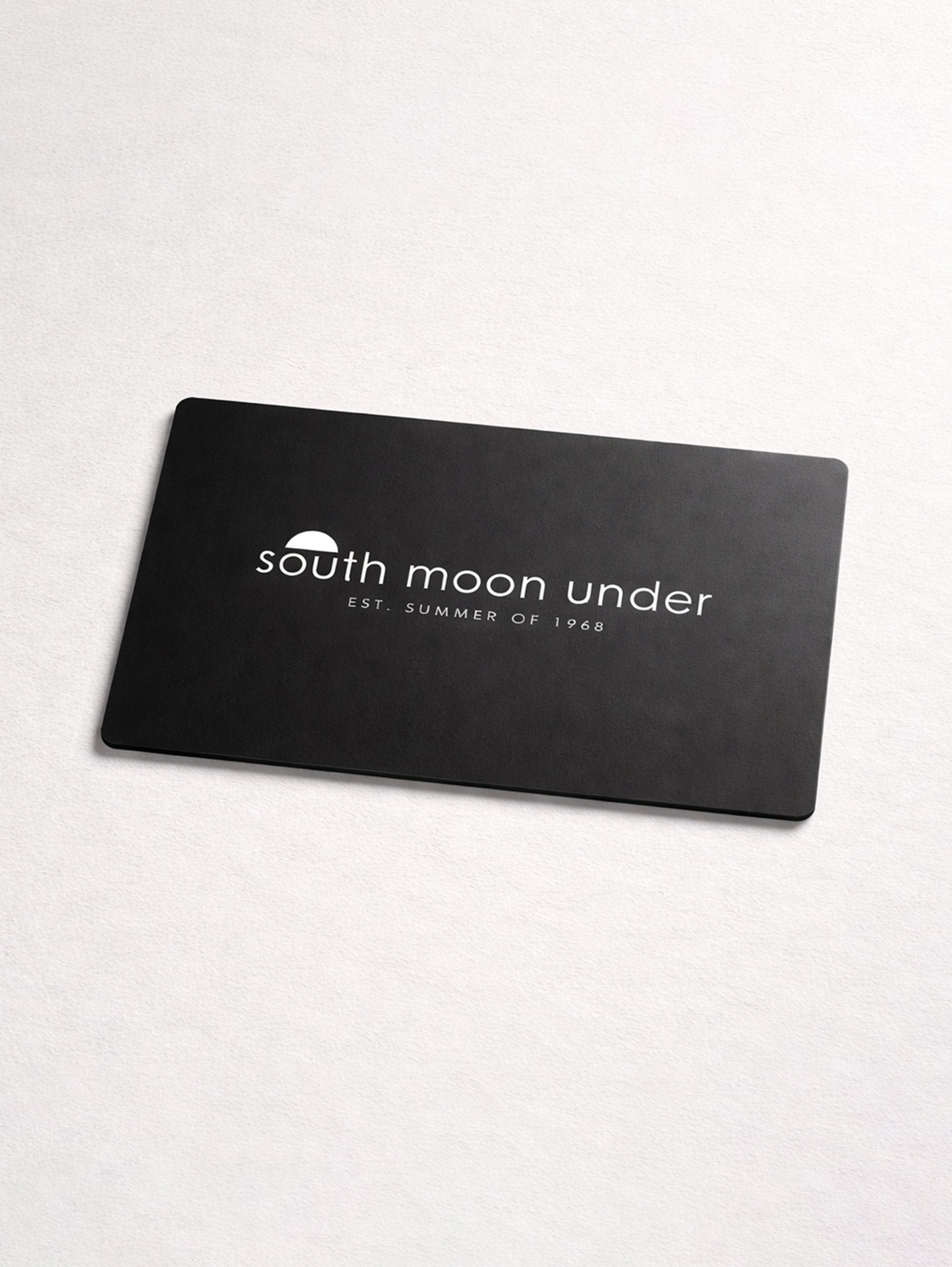 A black rectangular South Moon Under eGift Card with a white logo and "EST. SUMMER OF 1968" is centered on a light surface.