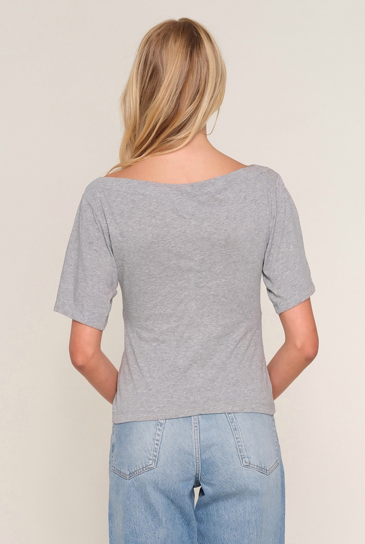 Back view of a blonde woman wearing the Heartloom Monique Top, a slim fit grey boat-neck t-shirt, paired with light wash denim jeans.