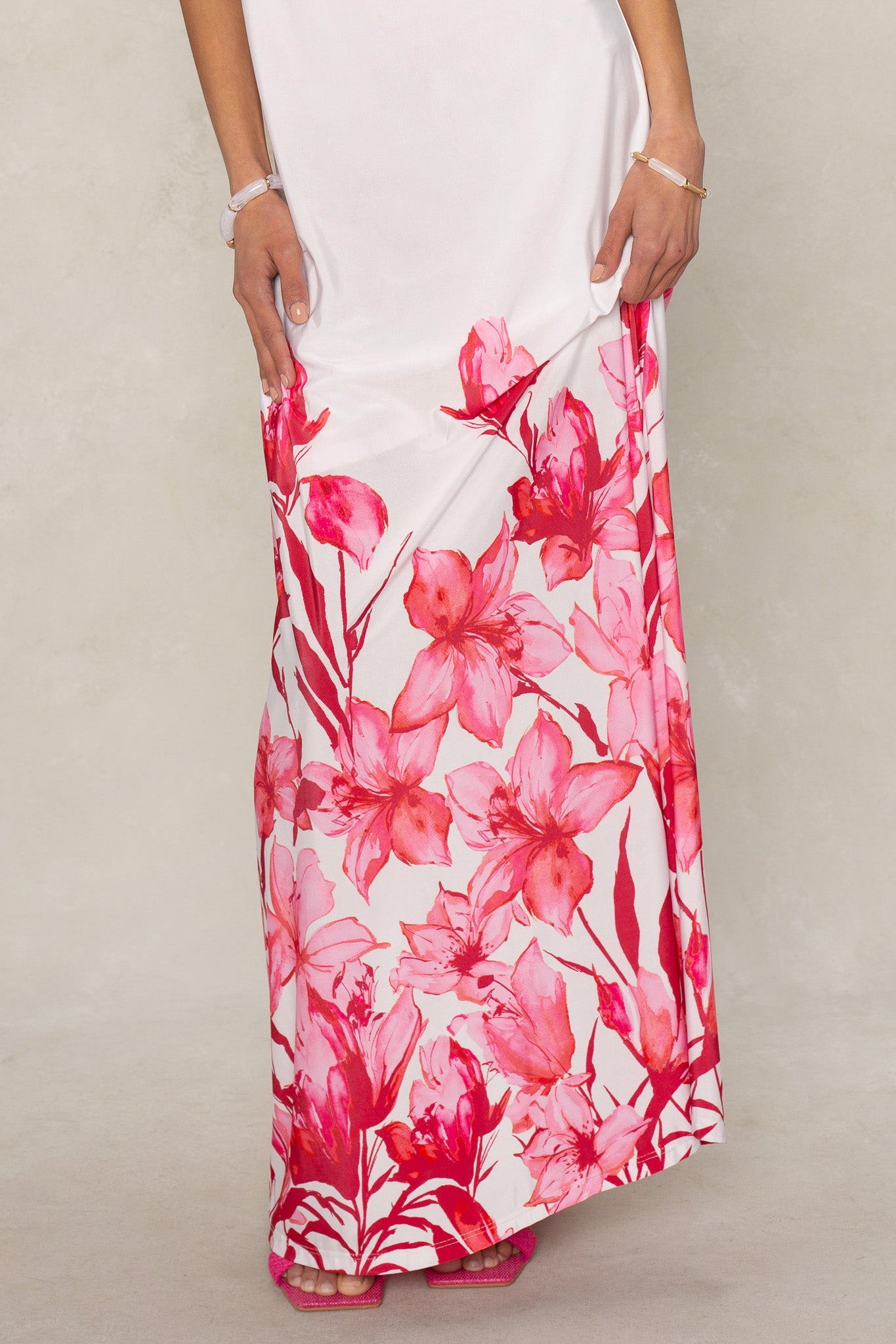 A person stands against a light background wearing the Isla Flora Tube Maxi Dress, featuring bright pink and red floral patterns. Their hands are resting at their sides.