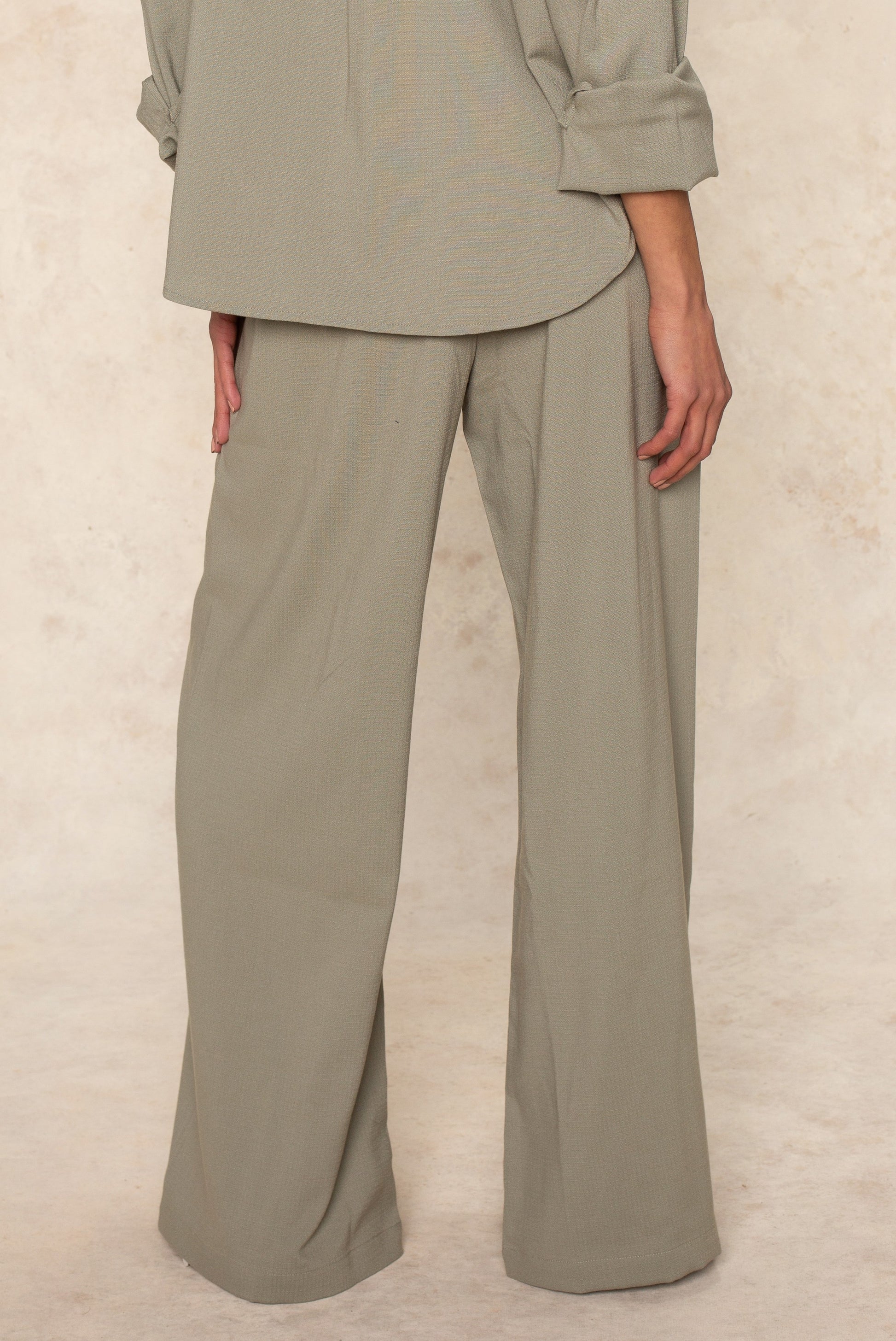 A person faces away from the camera, showing only their lower torso and legs in Georgie's Seaside Pant—a loose-fitting, light gray, wide-leg style designed for breathable comfort and casual summer outings.