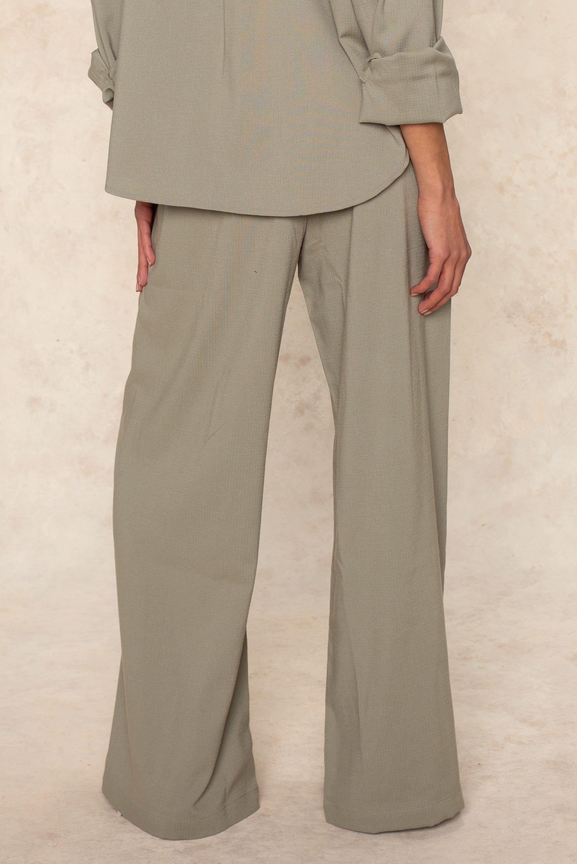 A person faces away from the camera, showing only their lower torso and legs in Georgie's Seaside Pant—a loose-fitting, light gray, wide-leg style designed for breathable comfort and casual summer outings.