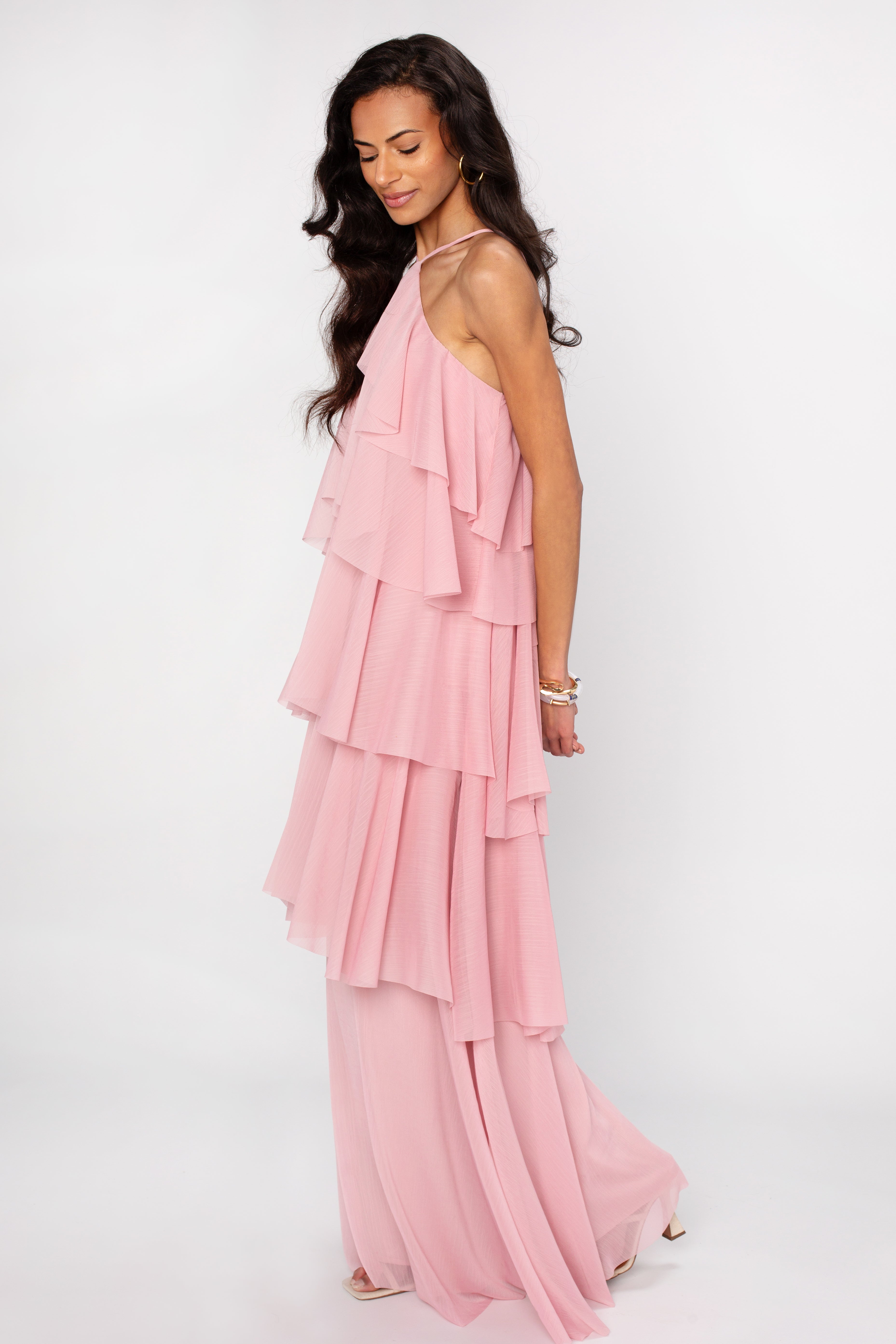 A woman with long dark hair wears the Georgie Ophelia Ruffle Tiered Maxi Dress and white heels, standing sideways against a plain white background.
