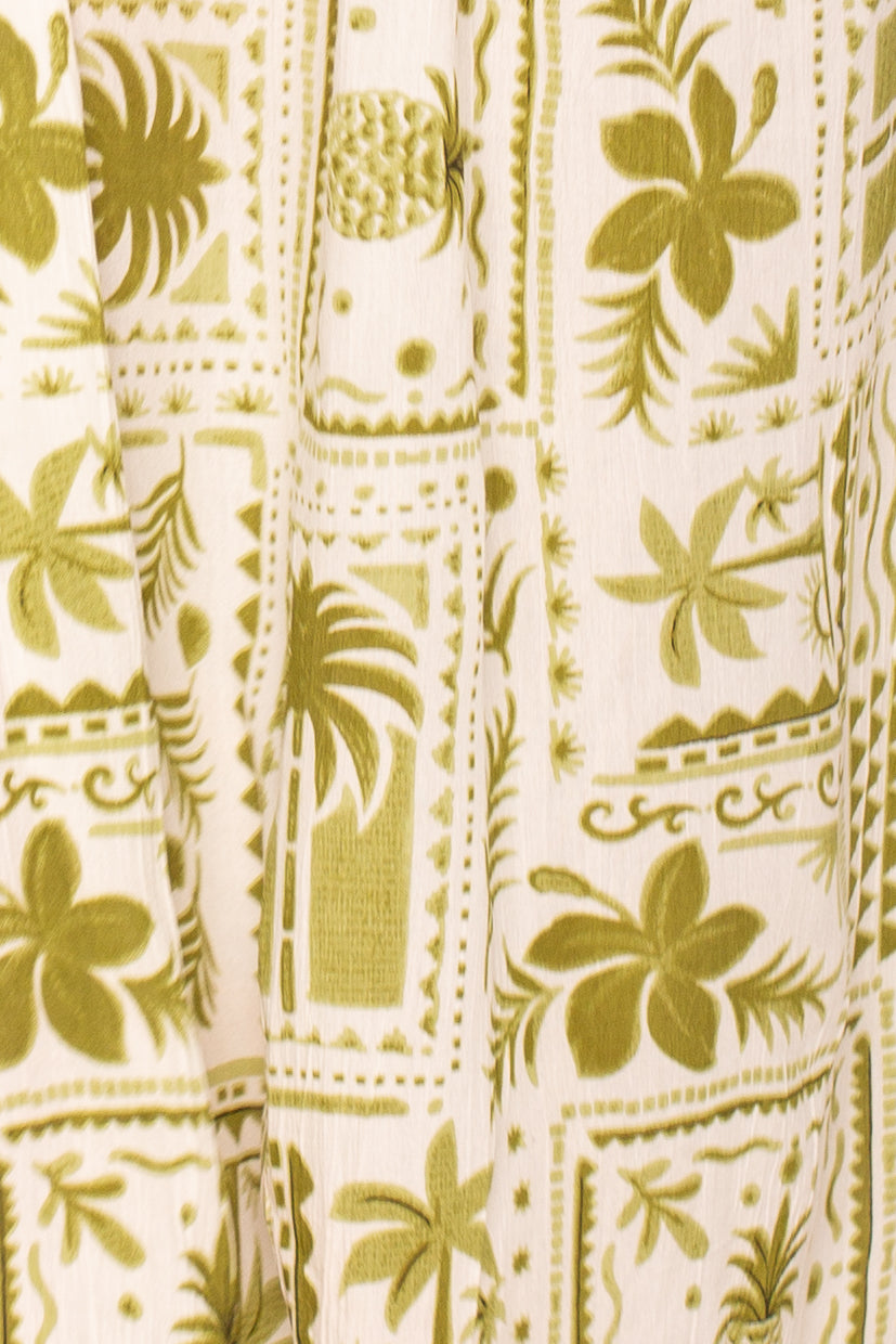 Close-up of Isla’s Postmark Maxi Dress Coverup fabric, showcasing an olive green tropical print with palm trees, flowers, pineapples, and geometric borders on cream—ideal for effortless beach-to-resort style.