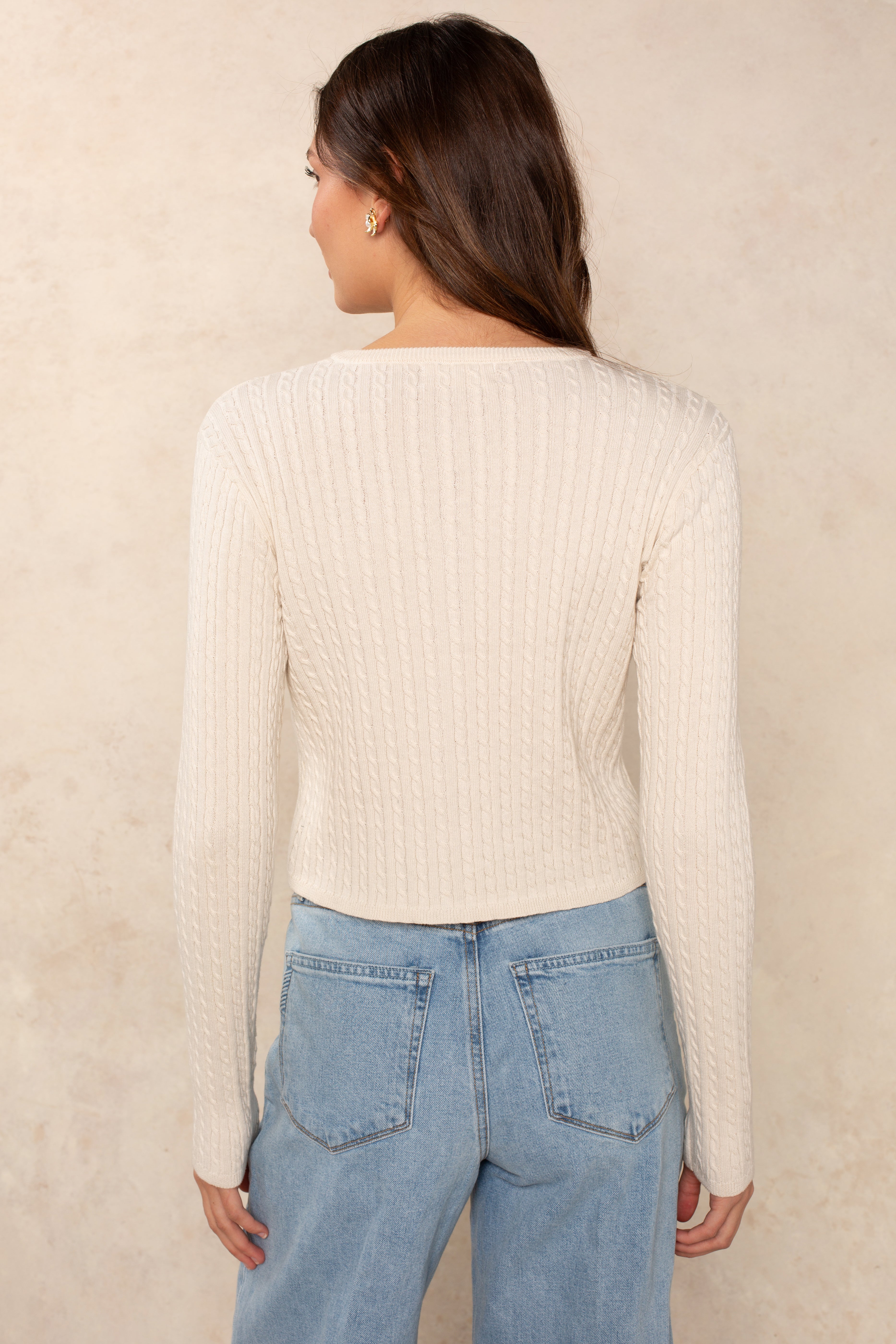 Back view of a woman wearing the Georgie Evonne Cable Cardi in cream with a cropped silhouette, paired with light wash denim jeans.