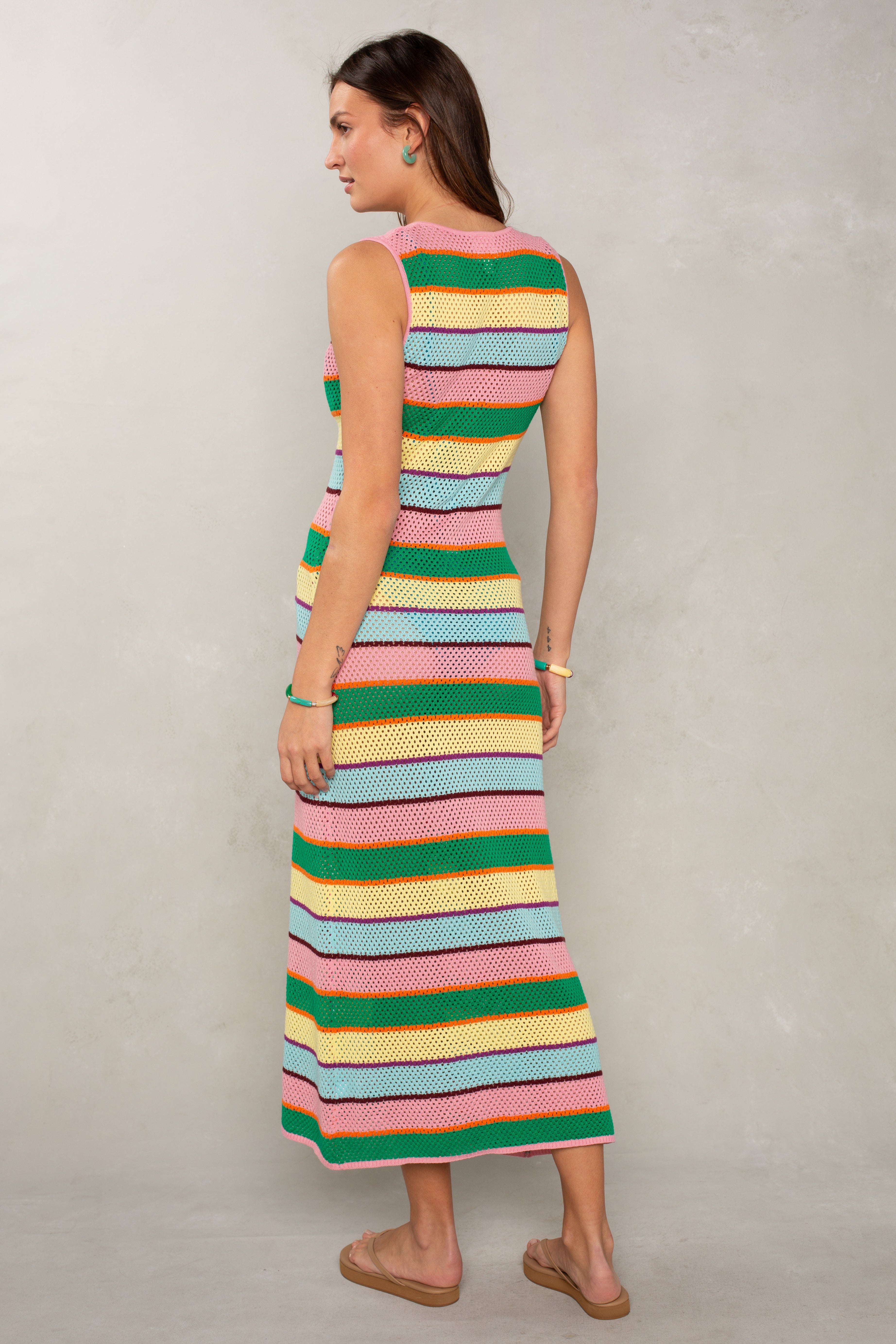 A woman stands sideways wearing the Isla Jessa Crochet Stripe Tank Maxi Coverup, a sleeveless, ankle-length piece with wide, colorful stripes—ideal breathable beachwear. She has long brown hair and tan sandals.