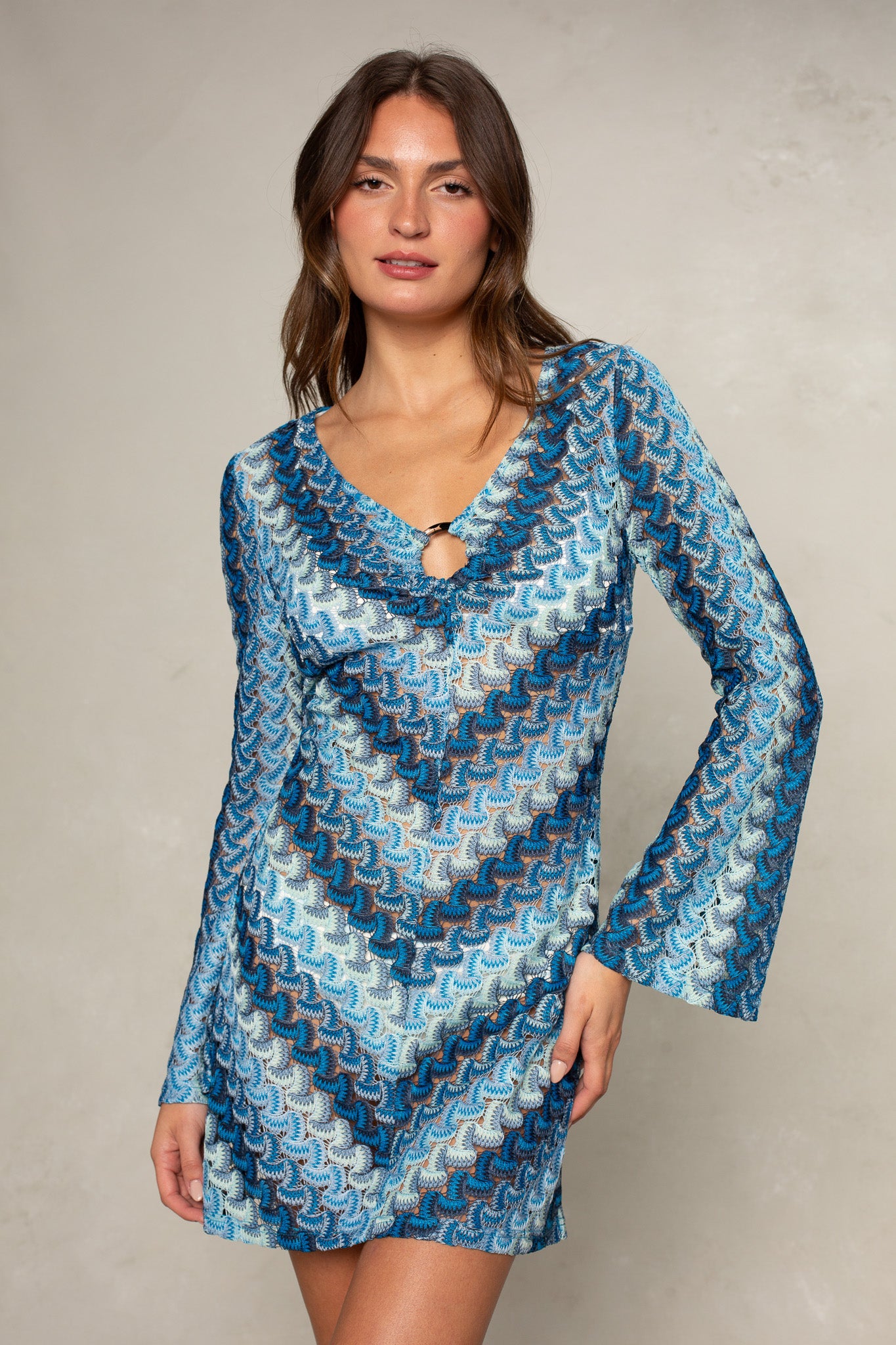 A woman wears the Isla Stella O-ring Mini Coverup in Blue Multi—a chic, patterned mini dress that doubles as a stylish swimwear coverup—standing against a light, neutral background.