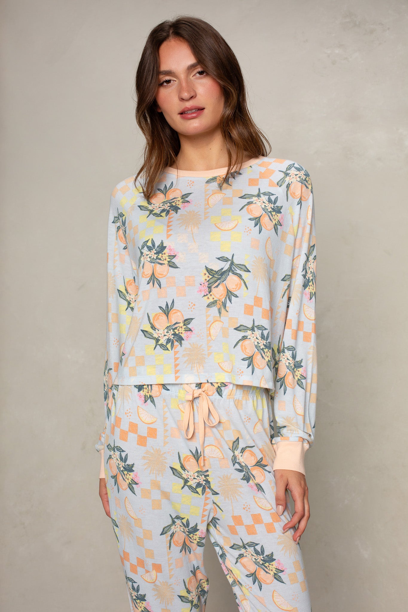 A woman wears Isla’s Citrus Check Brushed Jersey Top and matching drawstring pants, styled in a relaxed fit with a citrus and floral pattern, standing against a light textured background.