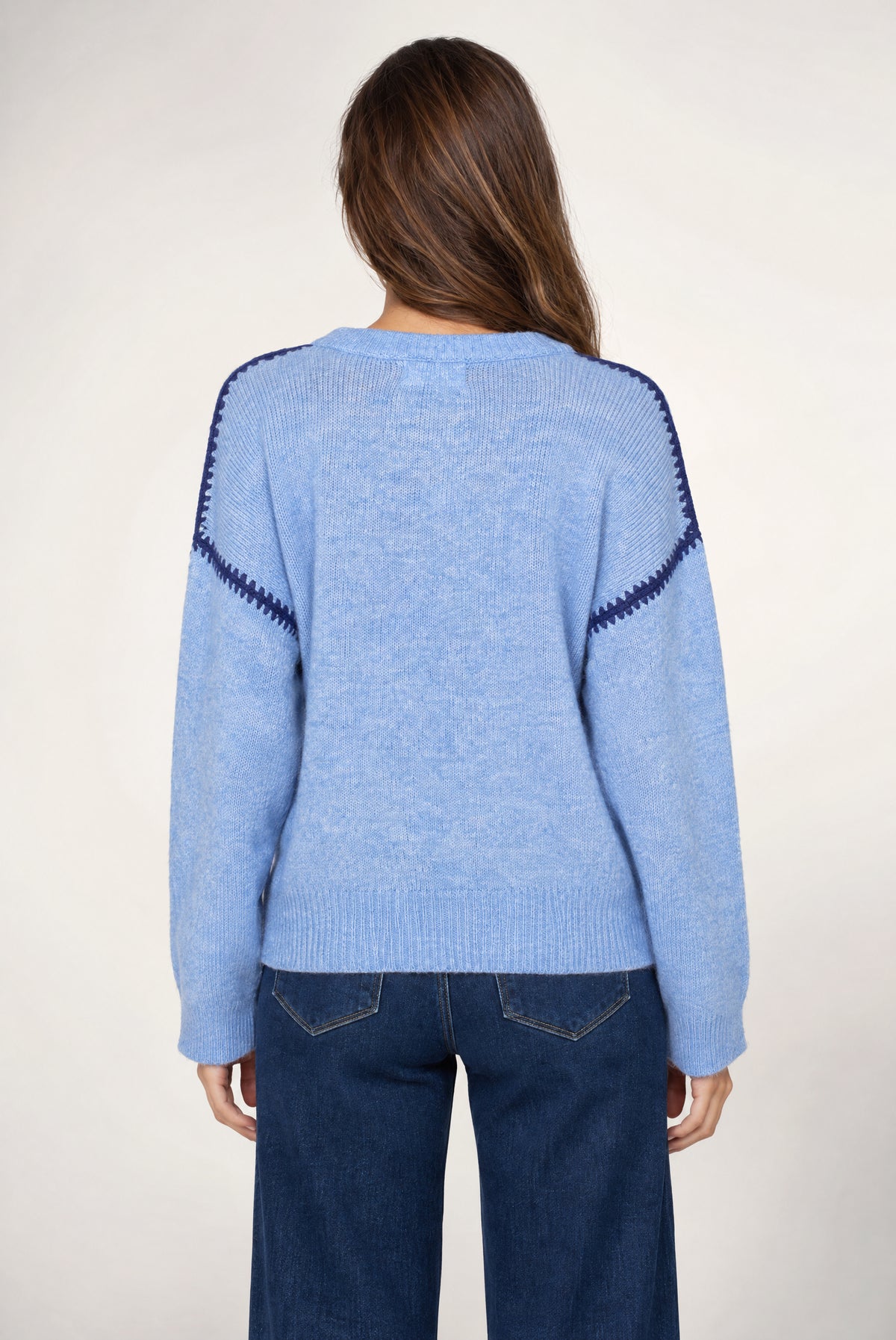 Light blue knit sweater with navy trim on shoulders and sleeves, shown from back on model wearing dark jeans.