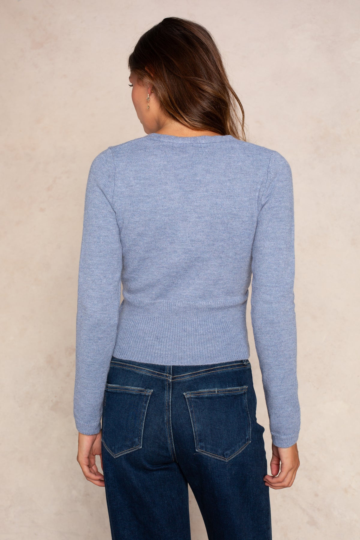 Woman wearing light blue fitted wrap sweater with long sleeves and dark blue jeans, shown from back.