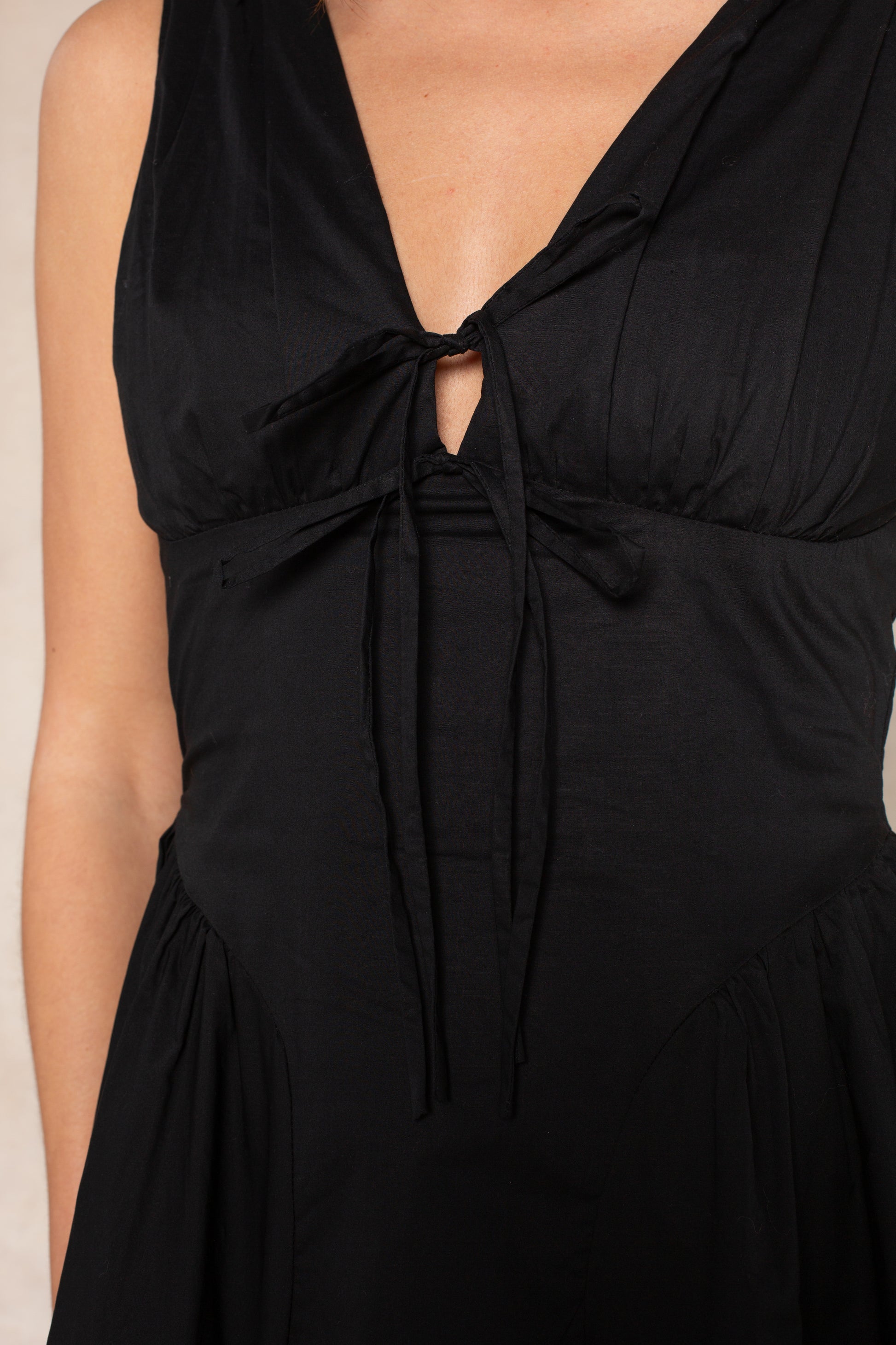 A close-up of a woman wearing the Georgie Vivianne Corset Midi Dress, featuring a sleeveless design, fitted bodice, deep V-neckline, and tied bow detail at the chest. Only her upper torso is shown.