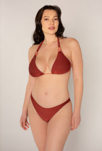 A woman with long dark hair poses confidently in the Amanda Batula Swim Brick Adjustable Triangle Top against a plain light background, facing forward with a relaxed expression and one hand by her side.