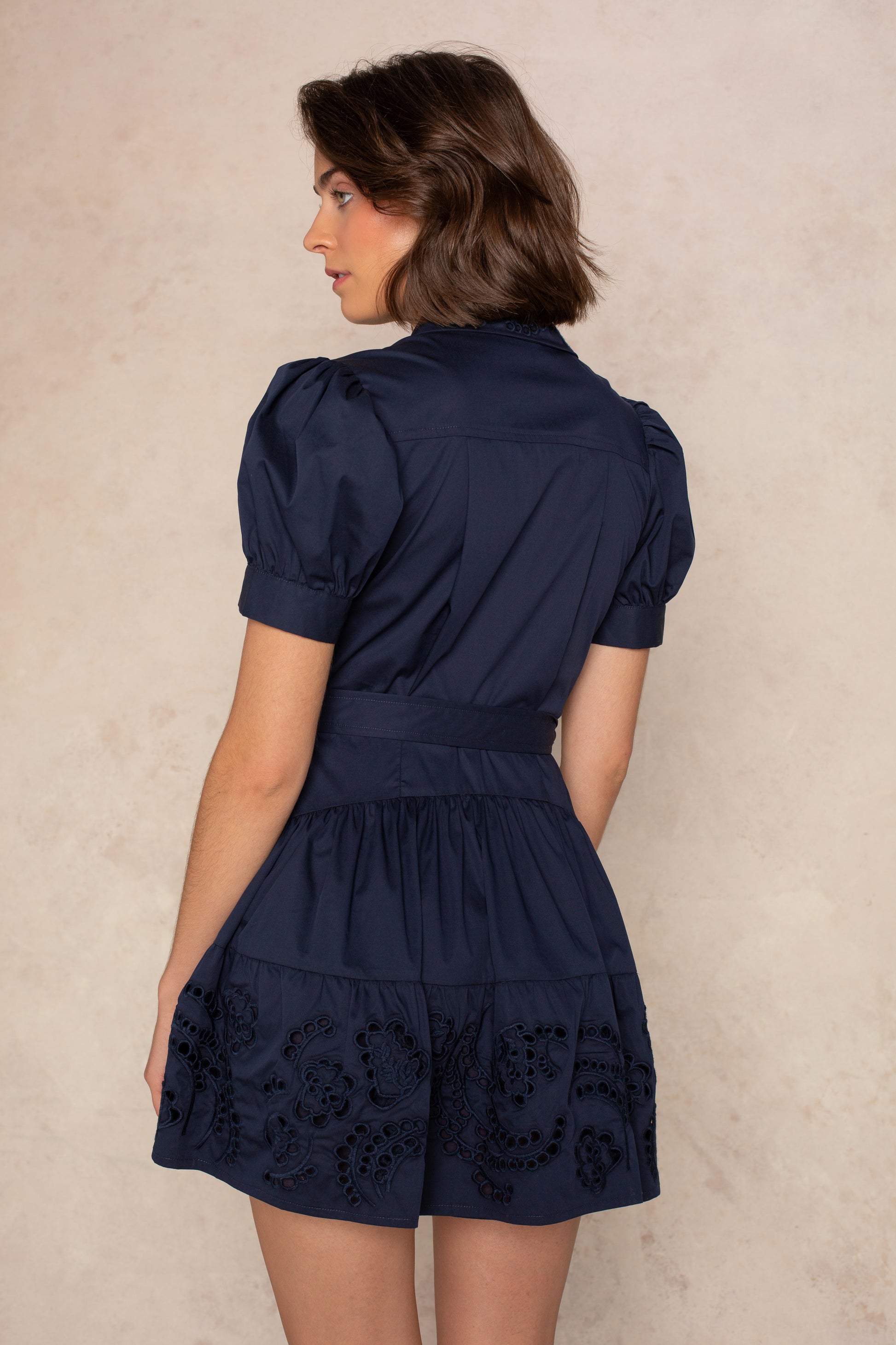 A woman with short brown hair wears the Georgie Madison Short Sleeve Mini Shirtdress, standing and looking left against a light beige textured background.
