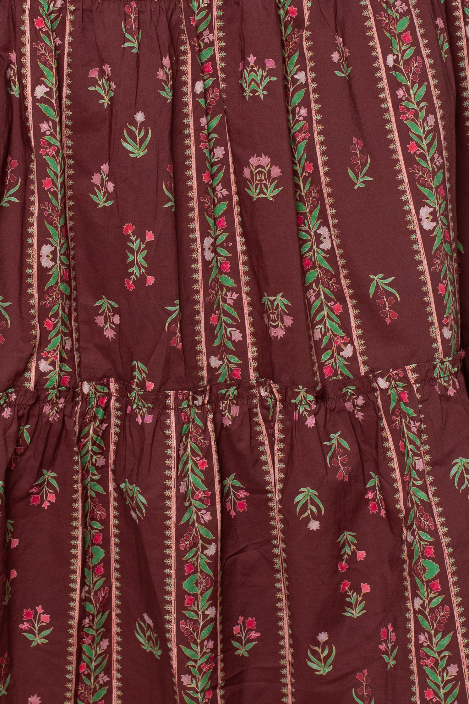 Close-up of the Melisse Maxi Skirt by Georgie, showcasing fabric with a maroon background and vertical stripes featuring green, pink, and white floral stripe print patterns accented by small decorative motifs. The texture is slightly gathered or ruched, capturing the relaxed and stylish bohemian appeal of this maxi skirt.