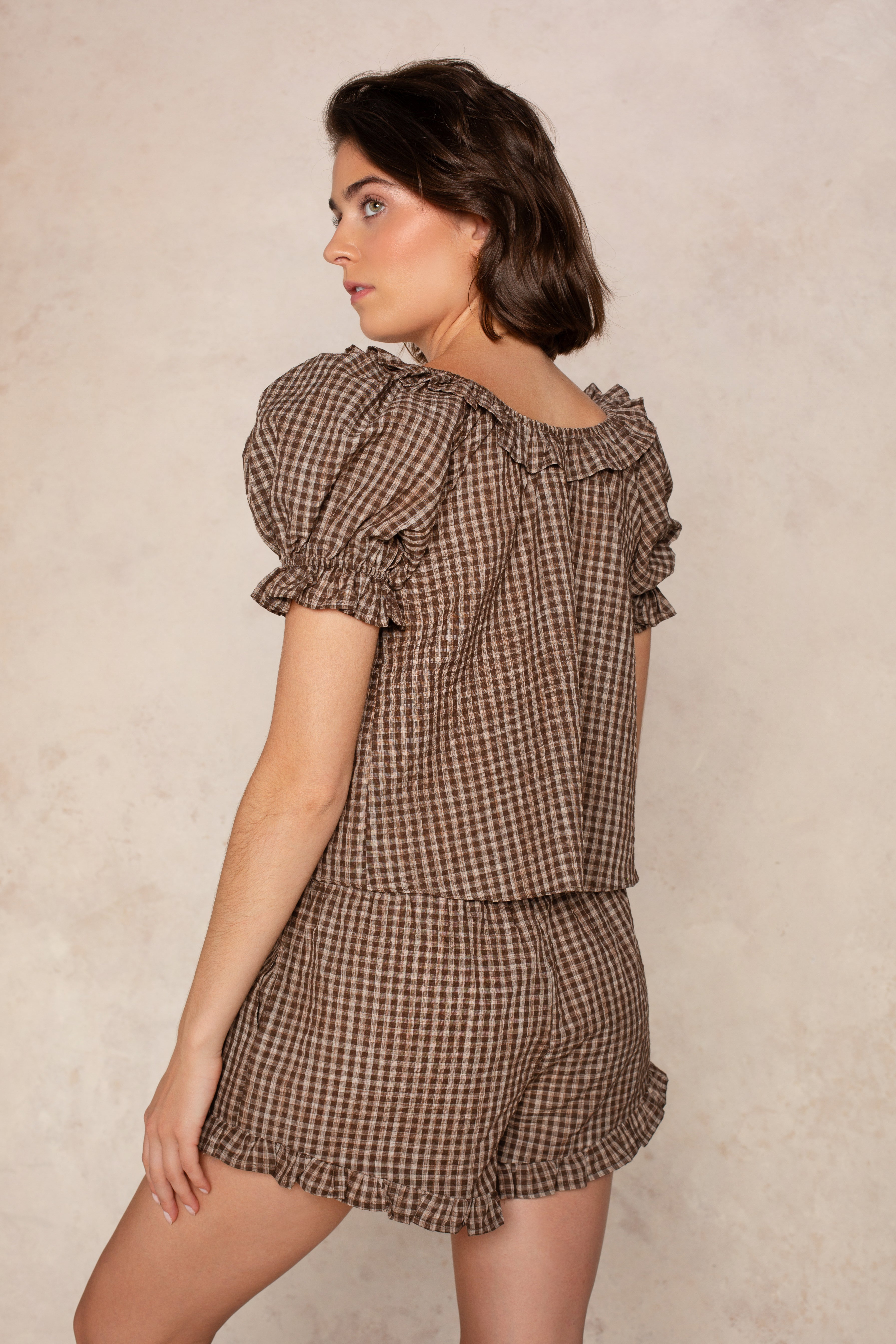 A woman with short brown hair models the Isla Ellie Plaid Gingham Set Short, standing sideways against a neutral background.