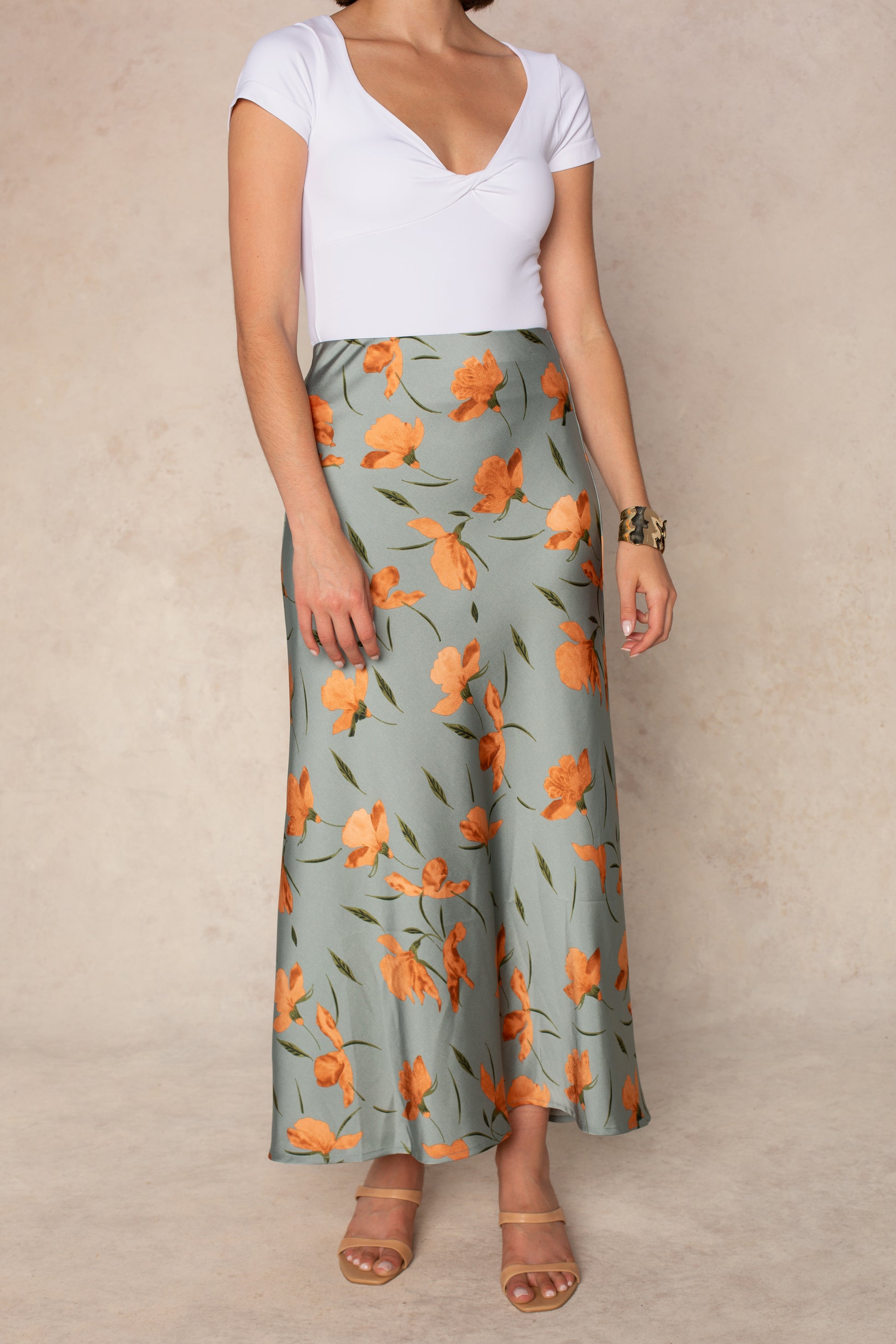 A woman wears a white short-sleeve top and the Georgie Emilia Satin Skirt in Blue Multi, styled with nude sandals and a bracelet.