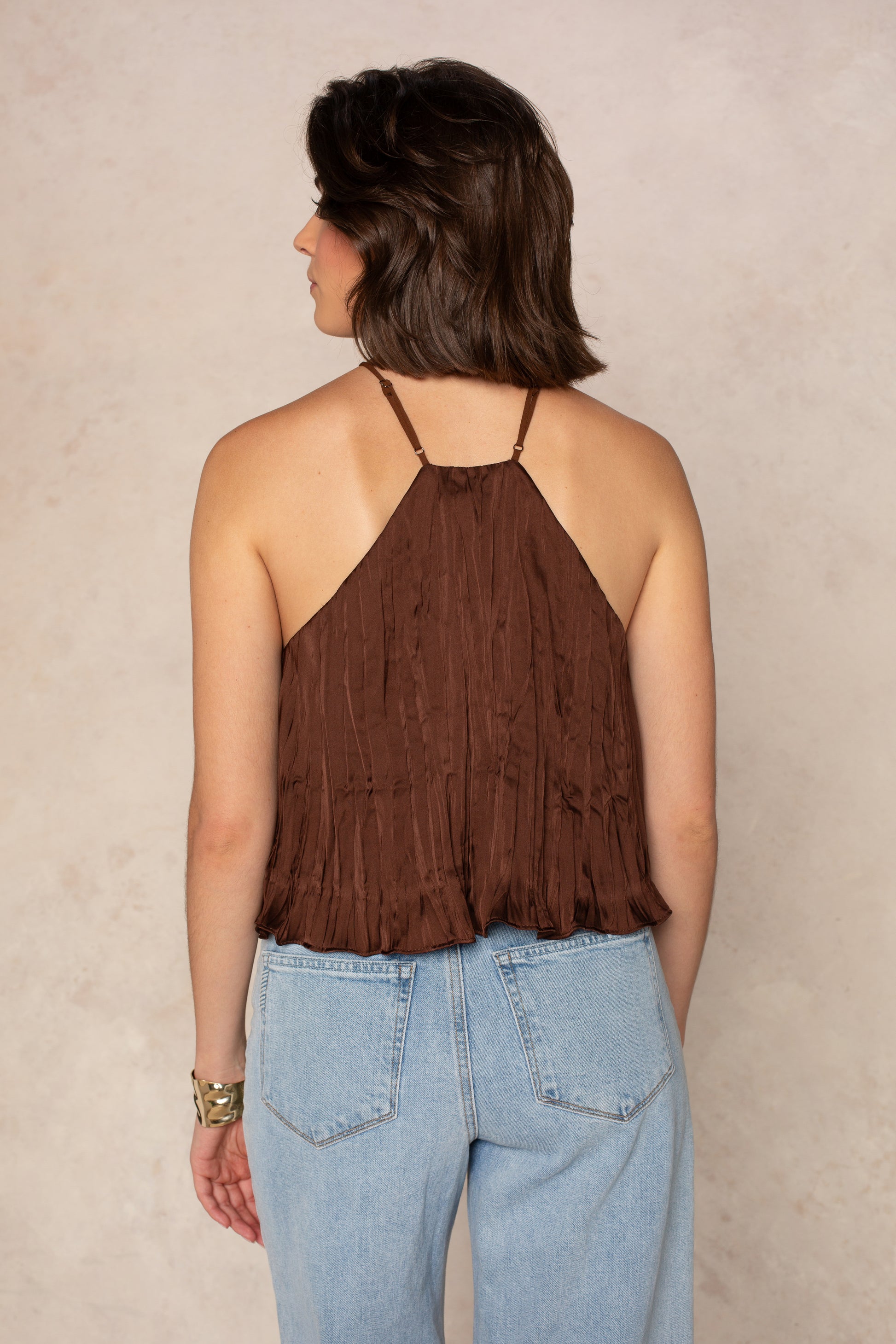 A person with short brown hair is shown from the back, wearing the Georgie Olivia Y Neck Halter in brown and light blue high-waisted jeans against a neutral beige background.
