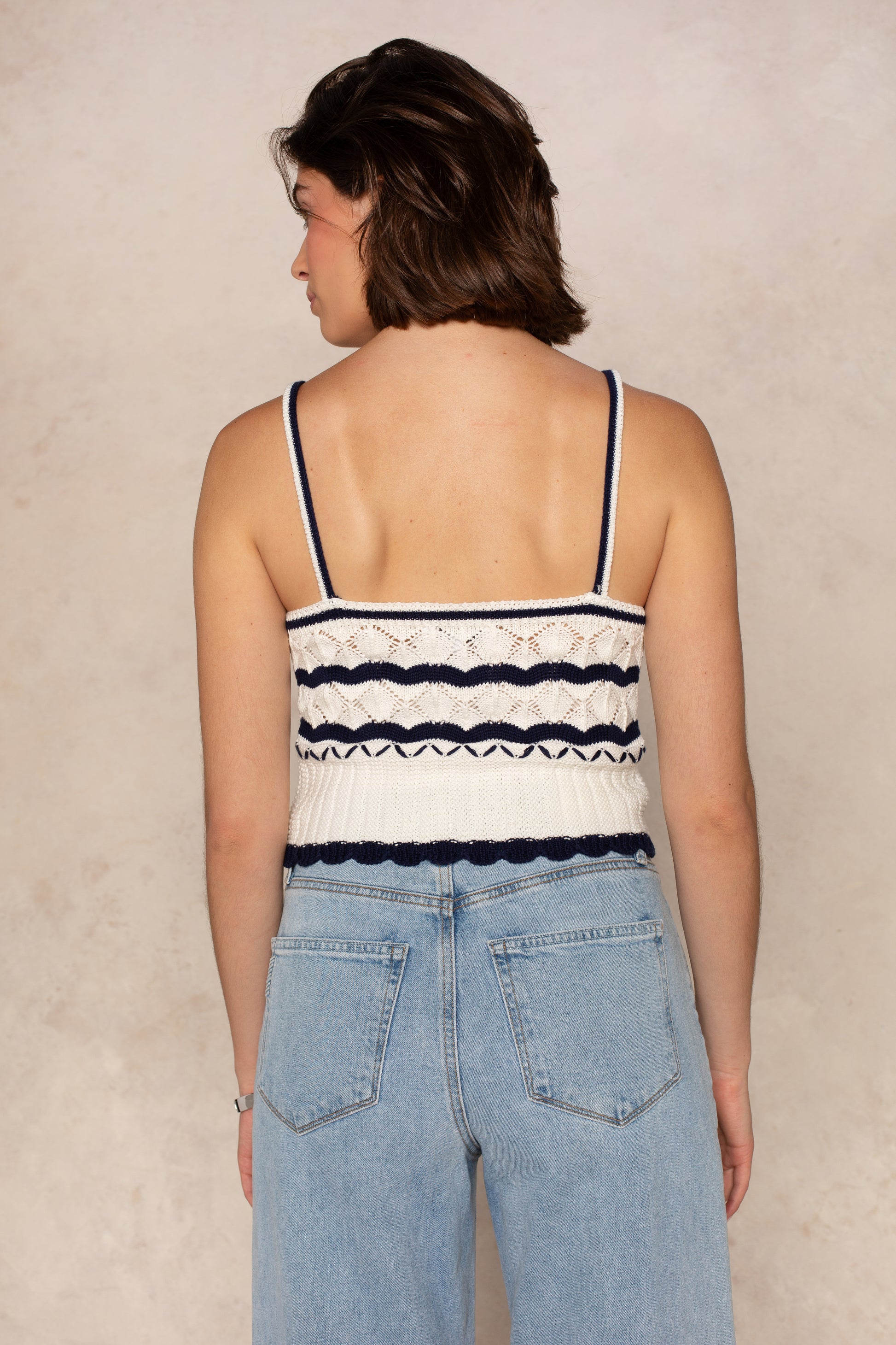 A person with short brown hair, wearing the Isla Layla Crochet Scallop Hem Tank and light blue high-waisted jeans, stands with their back to the camera against a neutral background.