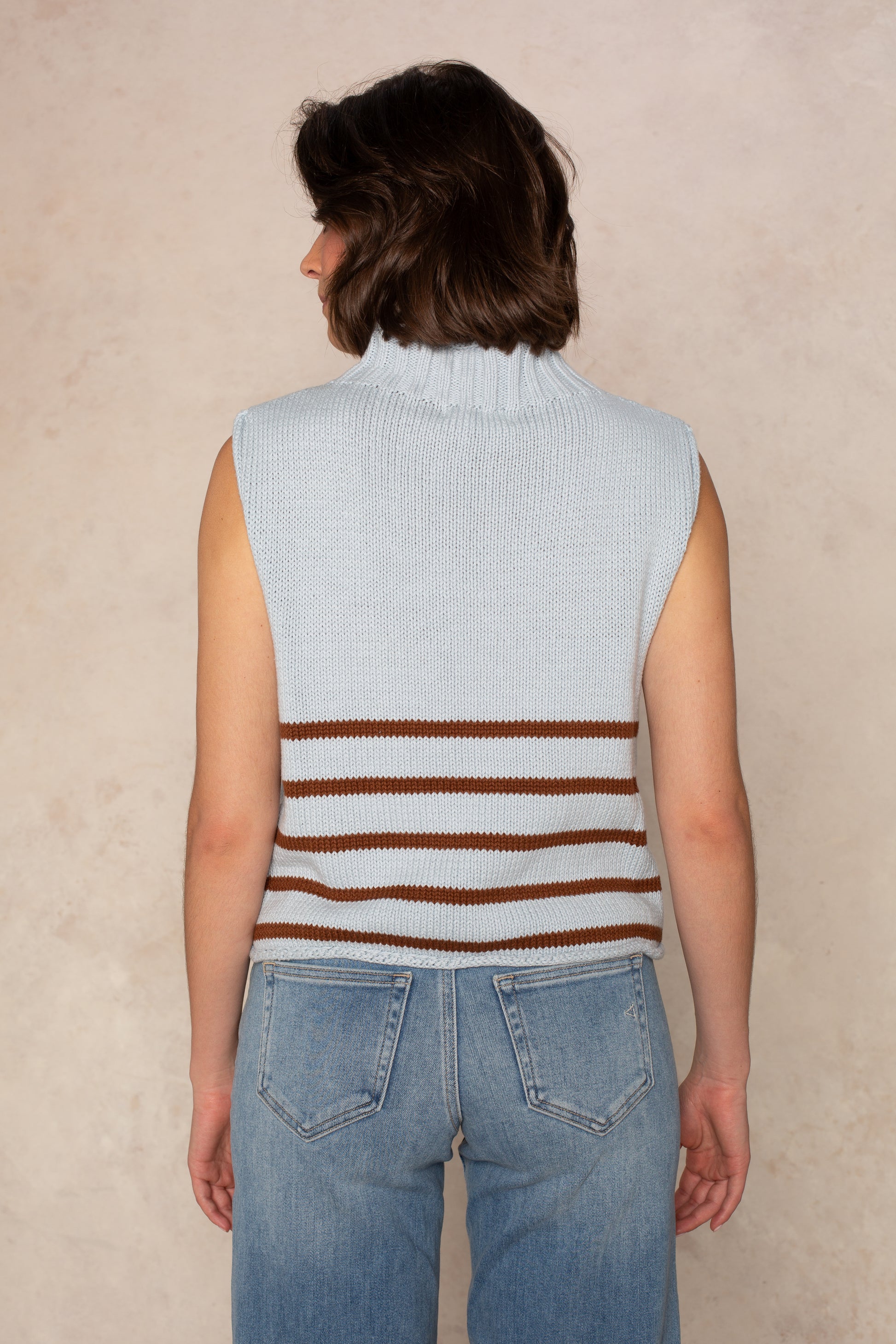 A person with short brown hair is shown from the back in the Georgie Grace Rolled Neck Sleeveless Sweater in Blue and blue jeans, standing against a neutral background.