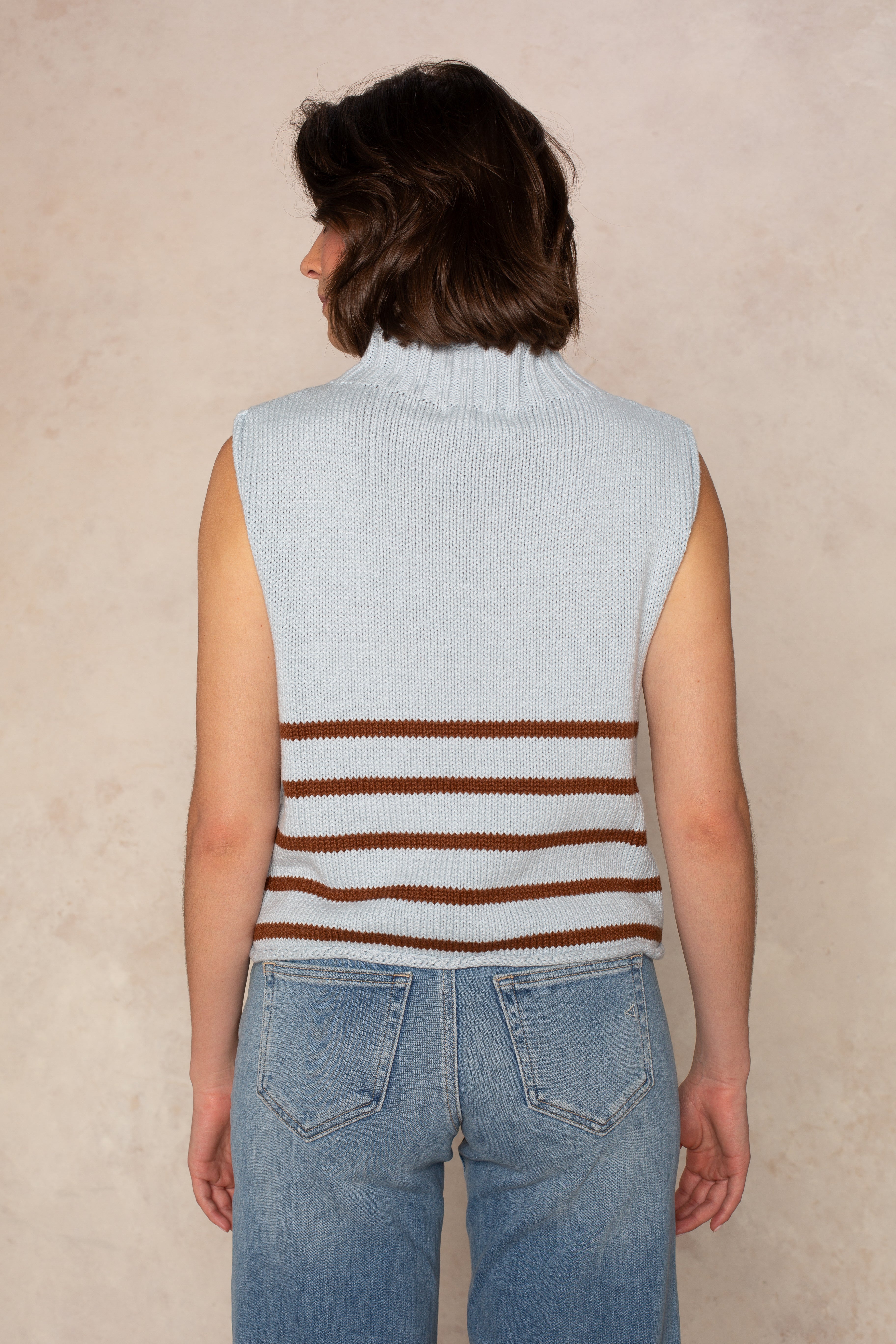 A person with short brown hair is shown from the back in the Georgie Grace Rolled Neck Sleeveless Sweater in Blue and blue jeans, standing against a neutral background.