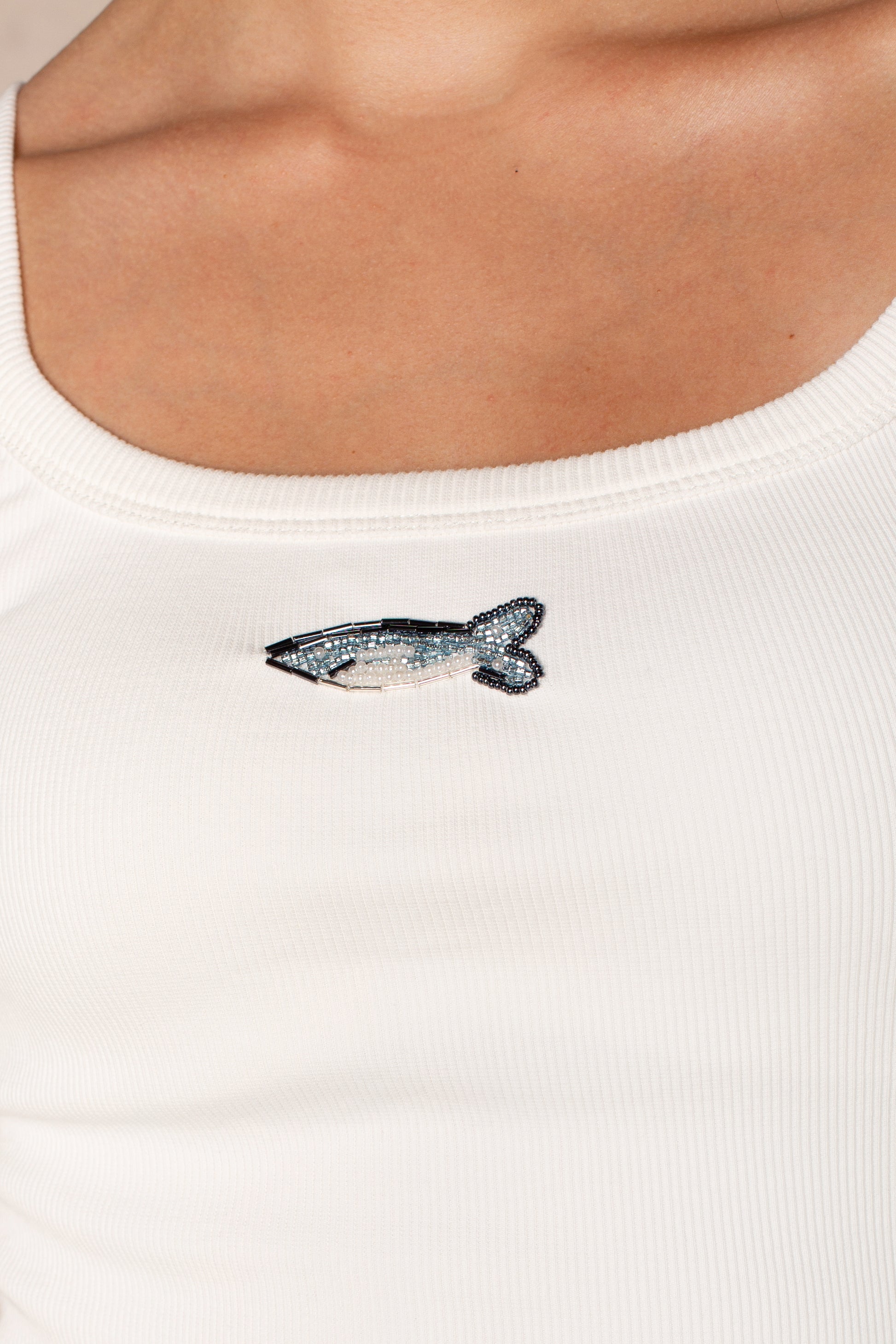 A close-up of a person wearing Isla's Fish Embroidered Vintage Fit Tank, featuring a blue and white beaded fish detail on the chest for a subtle coastal vibe.