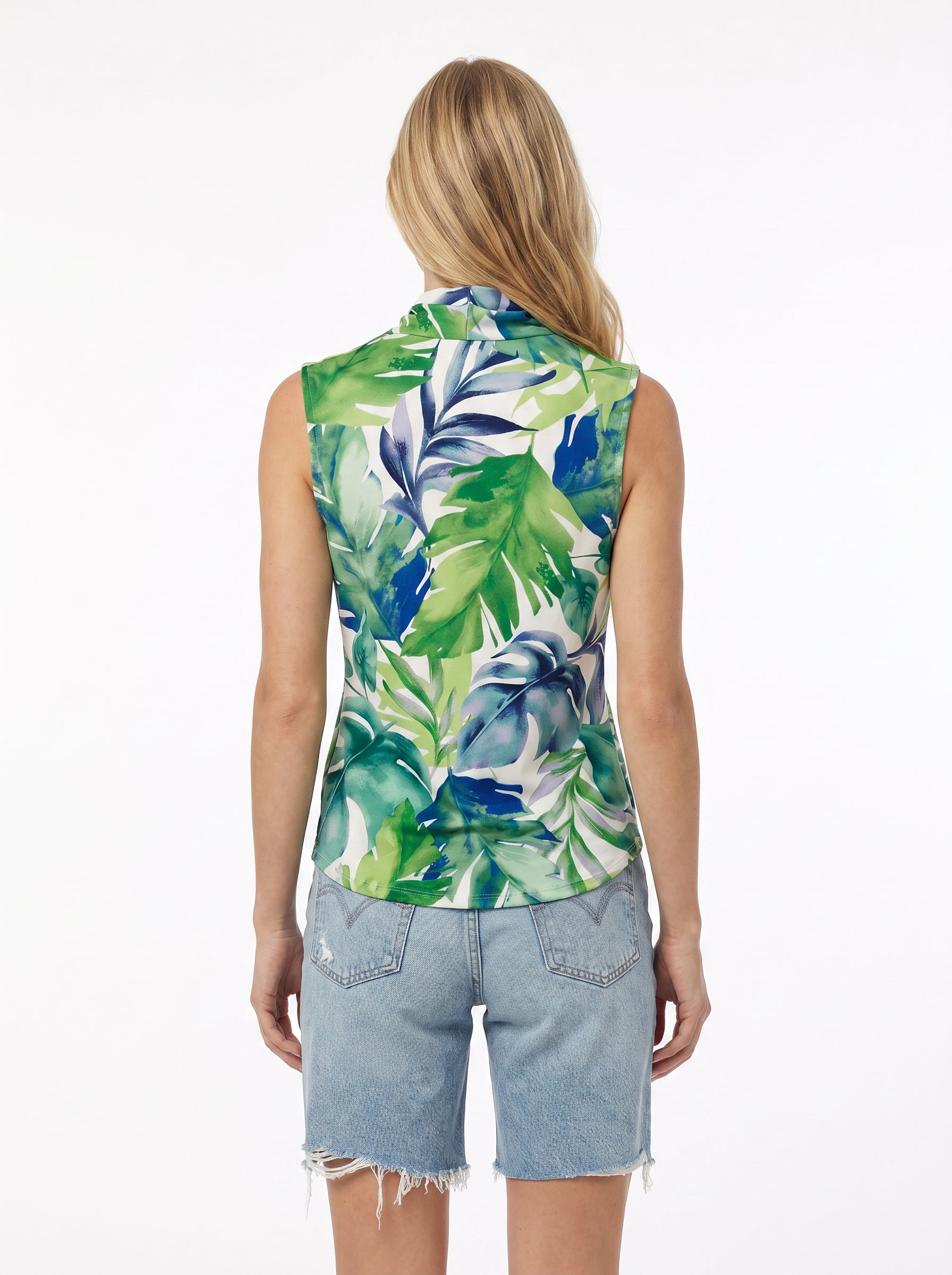 A person with long blonde hair is seen from the back, wearing the Georgie Gwen Sleeveless Wrap Top in a green and blue tropical leaf print, paired with light blue frayed denim shorts, standing against a plain white background.