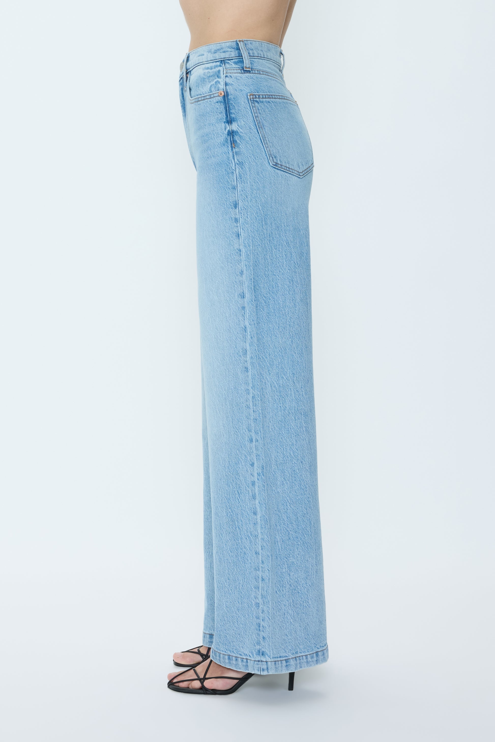 Someone wears the Pistola Lana High Rise Ultra Wide Leg comfort stretch jeans in light blue with black strappy heeled sandals, shown in side profile against a plain white background.
