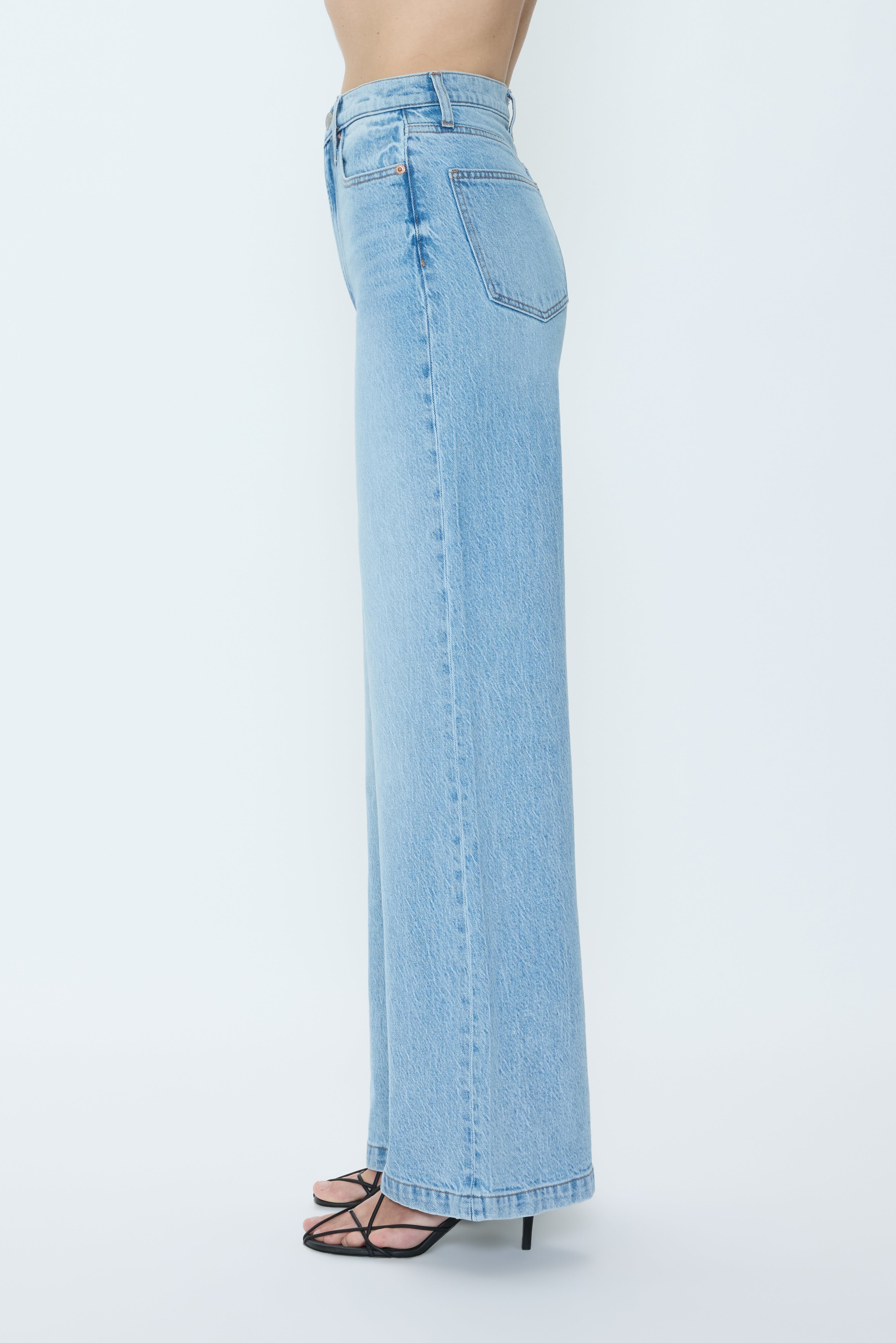 Someone wears the Pistola Lana High Rise Ultra Wide Leg comfort stretch jeans in light blue with black strappy heeled sandals, shown in side profile against a plain white background.