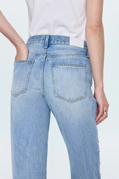 Wearing Pistola's Lexi In Confetti light blue, 100% cotton denim jeans with a relaxed fit, non-stretch, two back pockets, and a white waistband label, styled from the back with one hand in the pocket and a white t-shirt.