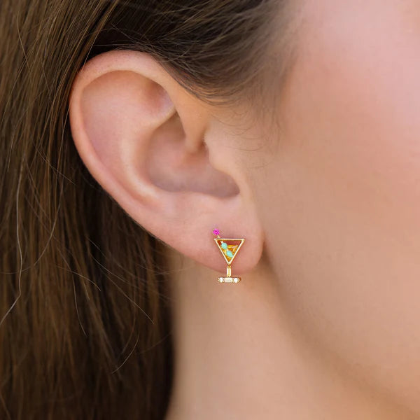 Close-up of a woman's ear wearing Girls Crew Martini Stud Earrings—18k gold plated, cocktail glass design with colorful cubic zirconia accents, including a pink stone—seen against brown hair and skin.