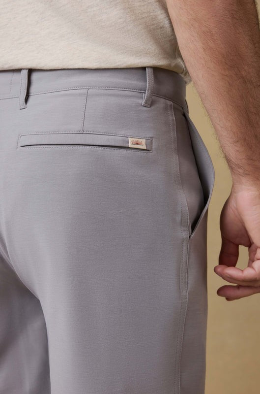 A close-up of a person wearing Faherty’s All Day Short 7 In in light gray and a beige shirt, with their right hand relaxed by their side, showcasing the shorts’ back pocket and side seam.