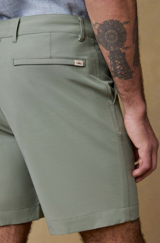 Someone wearing Faherty's All Day Short 7 In in light green and a light blue shirt, highlighting the back pocket detail, with part of their tattooed arm visible.