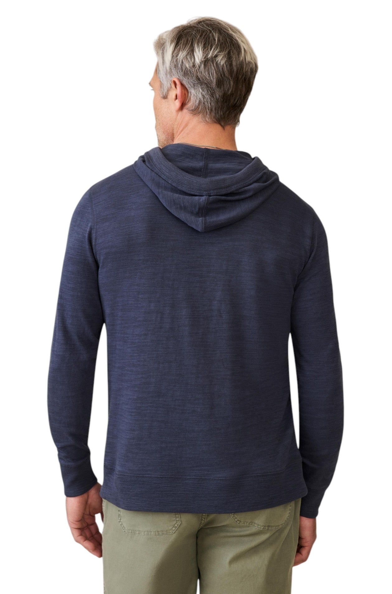 A man with short gray hair, wearing a Faherty Sunwashed Slub Hoodie in navy blue and light khaki pants, stands facing away from the camera against a white background.