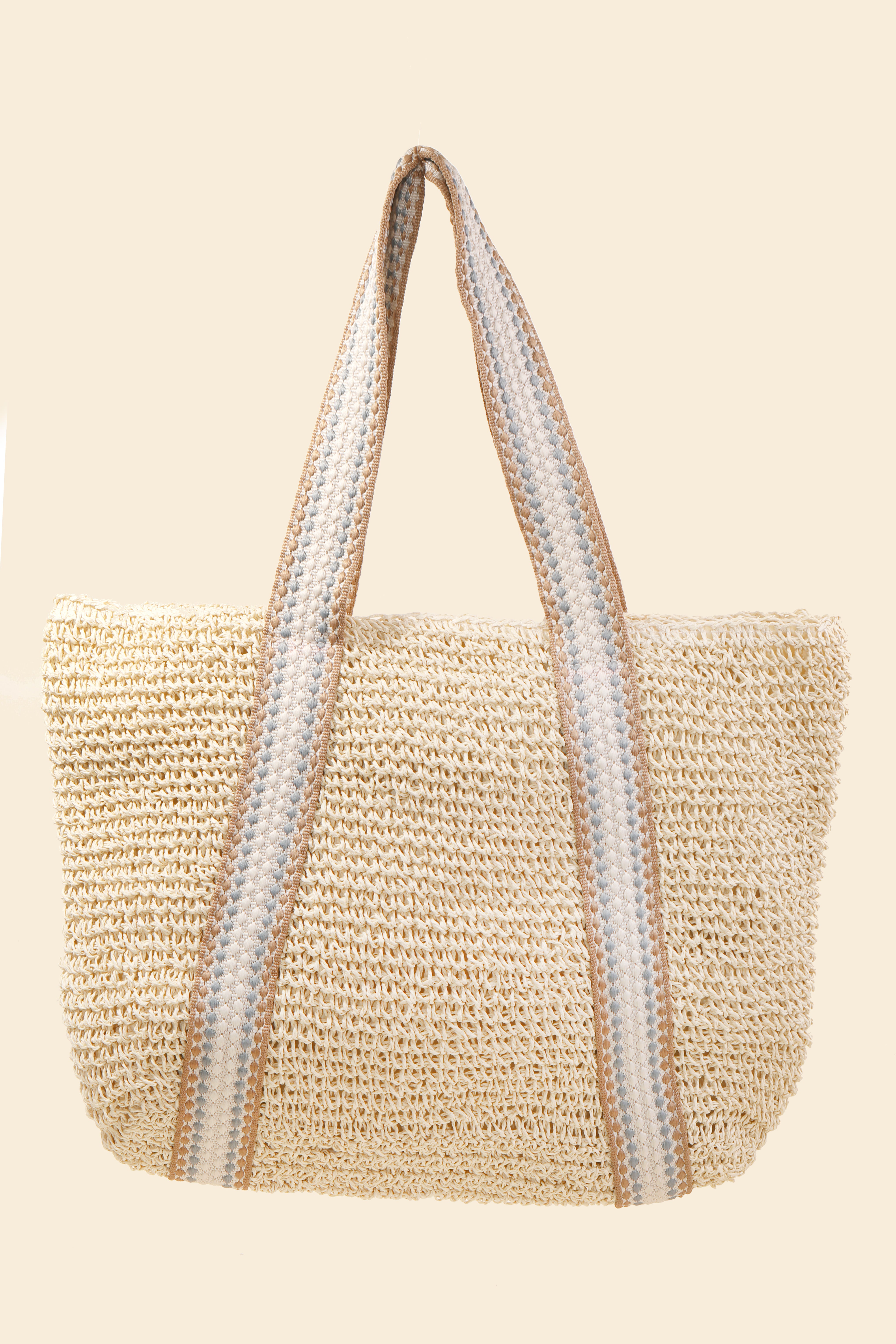 The South Moon Under Beach Tote is a woven straw bag with wide handles, featuring beige, white, and gray stripes in a classic paper style design against a light beige background.